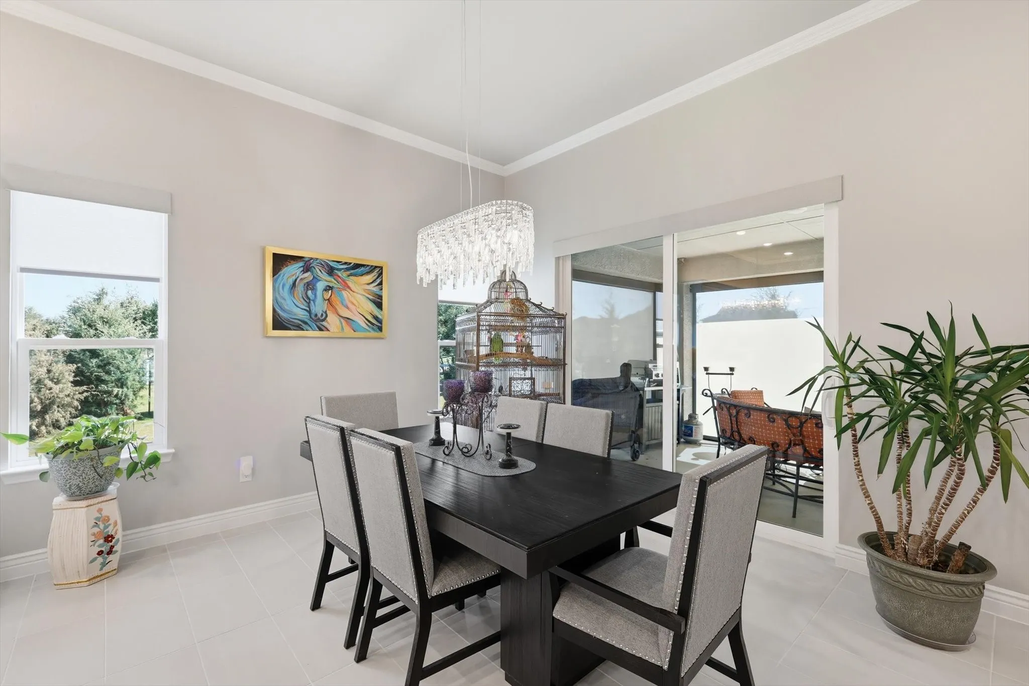 Dining area featuring tile flooring, crown molding, a rectangular chandelier, a window with exterior views, and sliding glass doors opening to an outdoor patio
