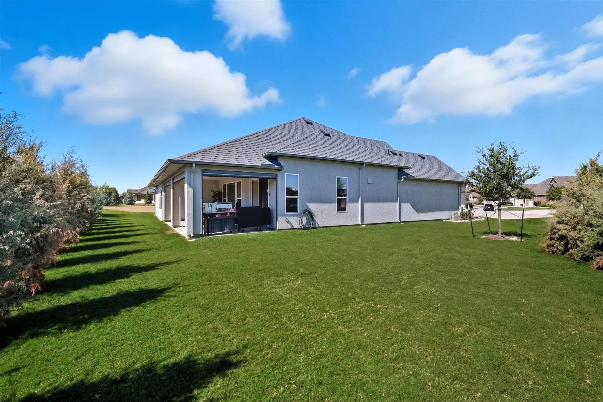Expansive green lawn with a covered patio, multiple windows, and a mature tree