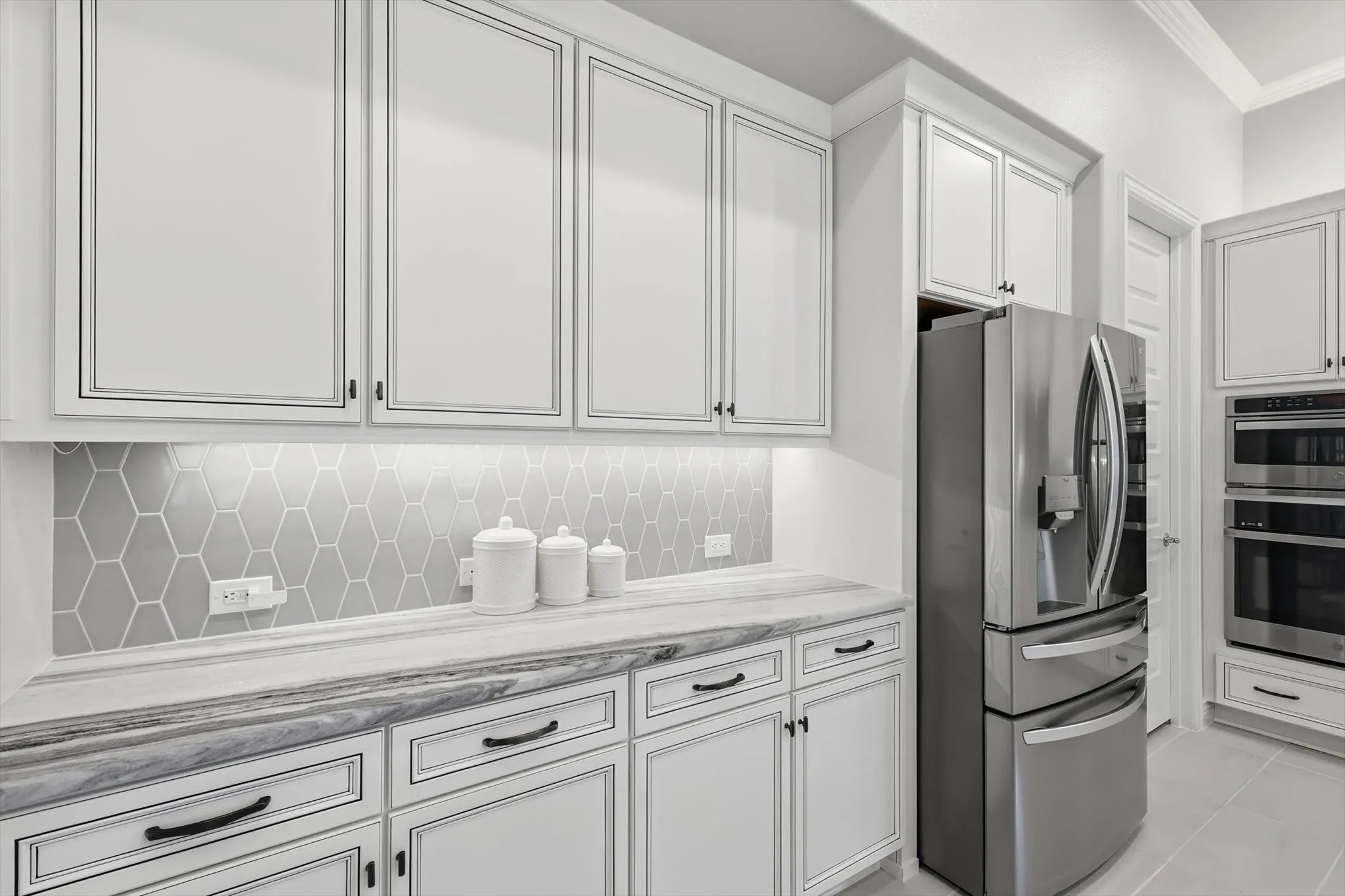 Kitchen featuring white perimeter cabinetry with black hardware, under-cabinet lighting, and a gray hexagonal tile backsplash
