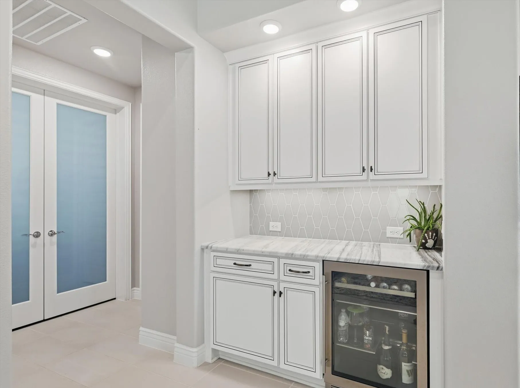 Built-in beverage station featuring white shaker cabinetry, marble-look countertops, and a full-height geometric tile backsplash