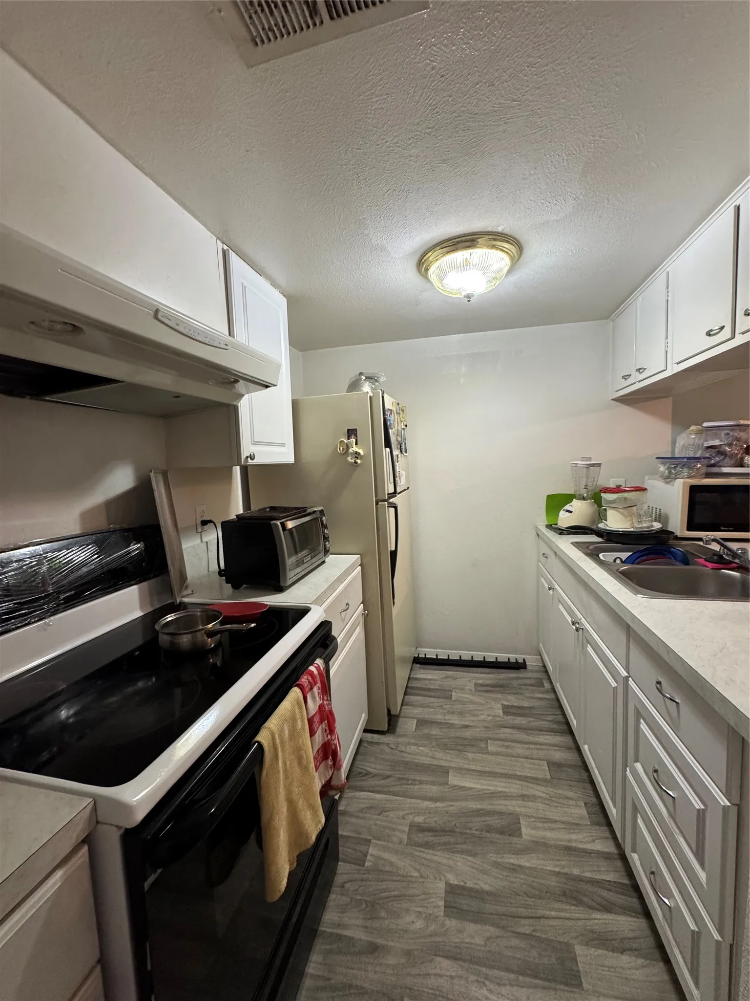 Compact kitchen featuring wood-look flooring, white cabinetry, integrated sink, and an overhead light fixture
