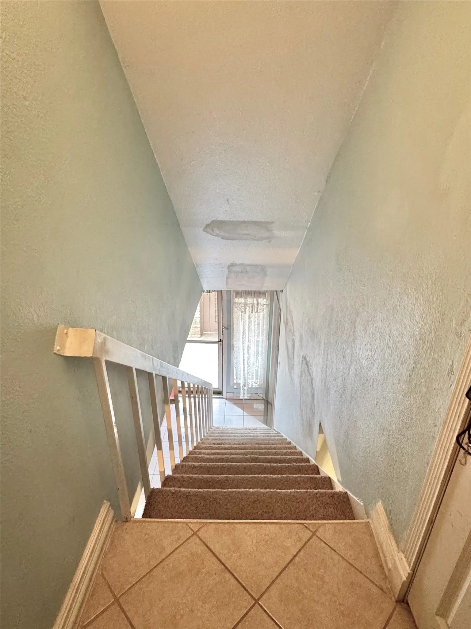 Staircase featuring diamond-patterned tile flooring, carpeted treads, and a white railing