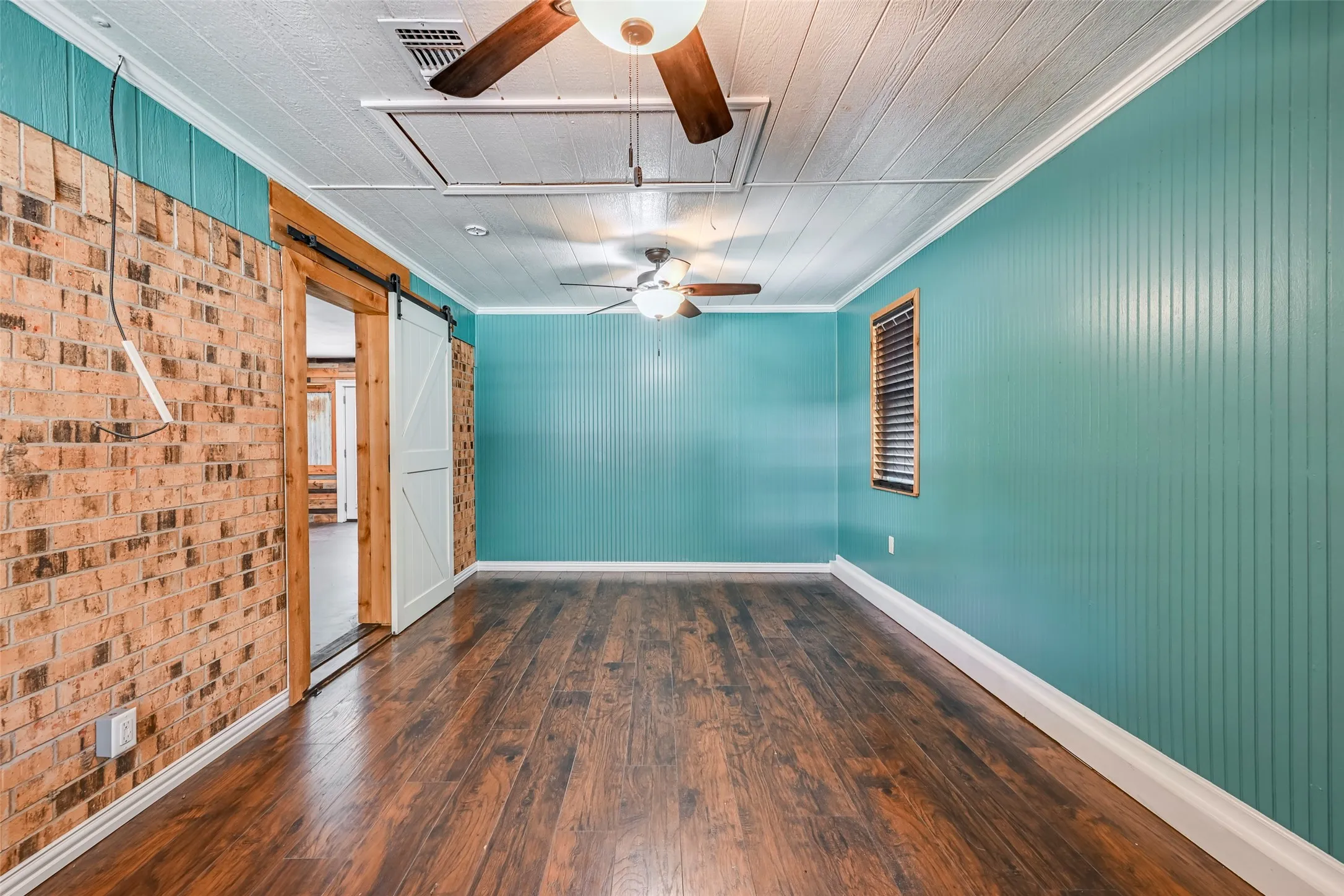 Spacious room featuring wood-finish flooring and a brick accent wall