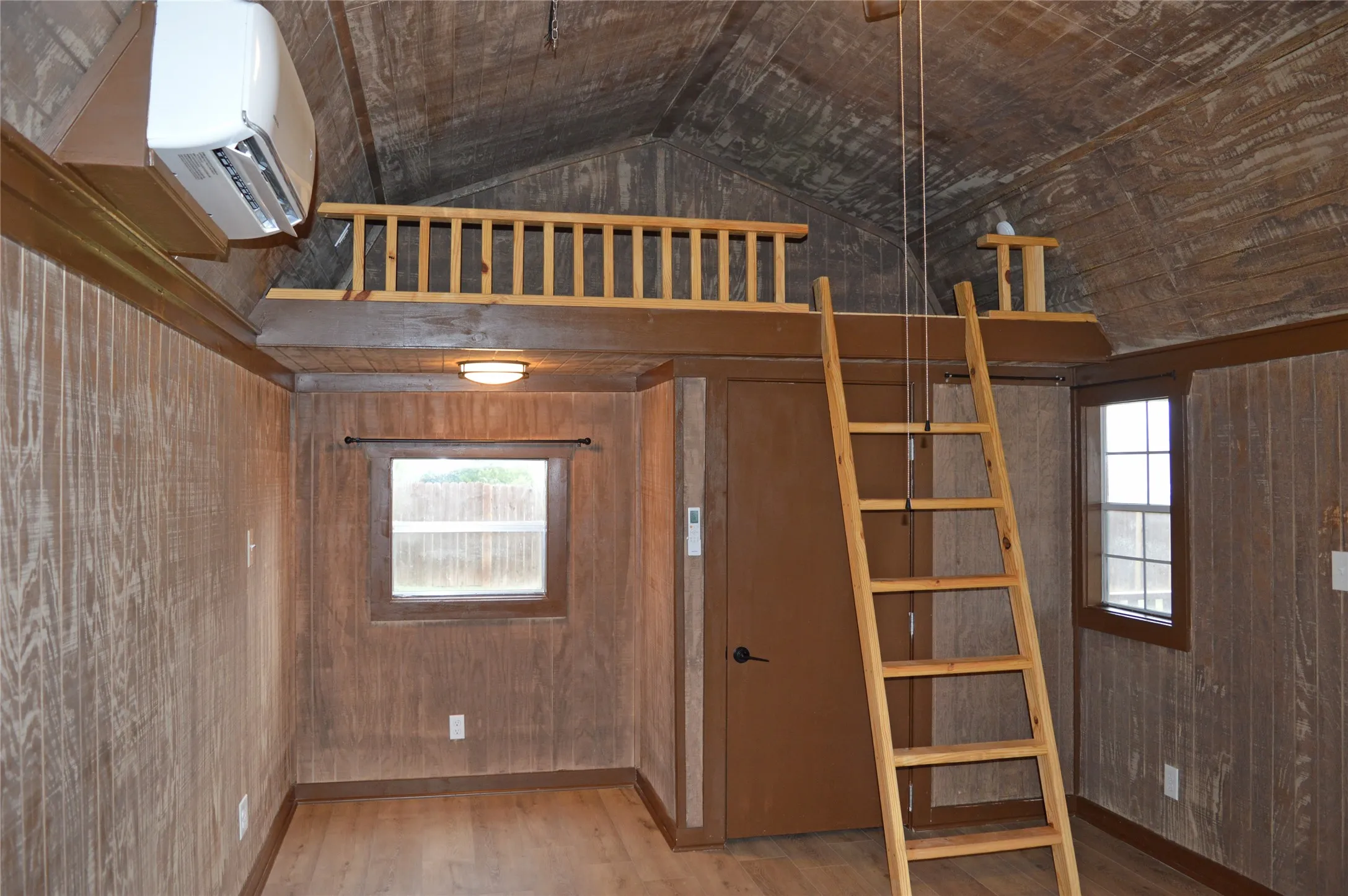 Interior space featuring wood-finish wall paneling, a built-in loft with wood railing, a portable wood ladder, and a window air conditioning unit