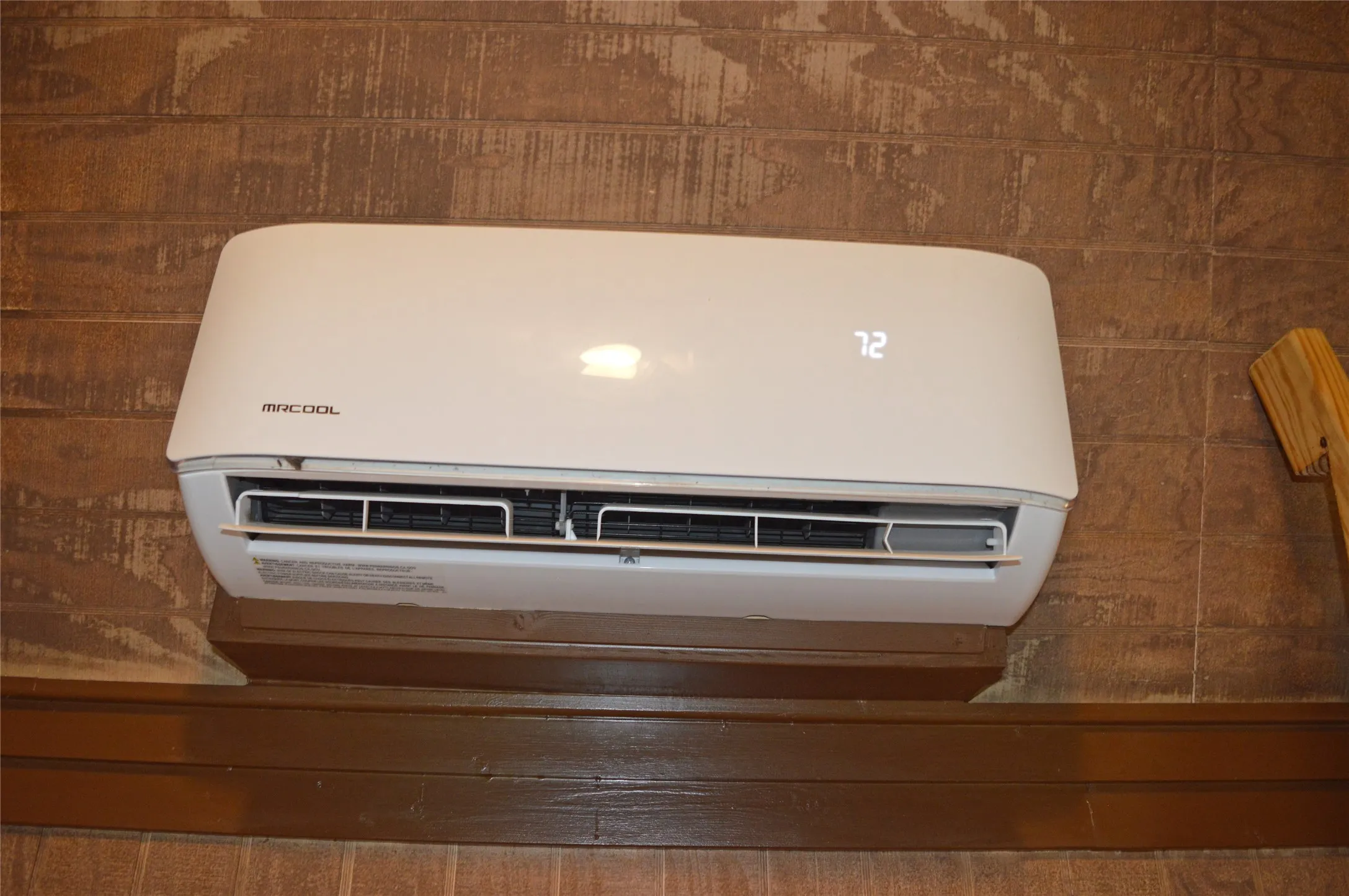 Wall-mounted mini-split system with digital temperature display, set against a distressed wood panel wall with a dark wood trim piece