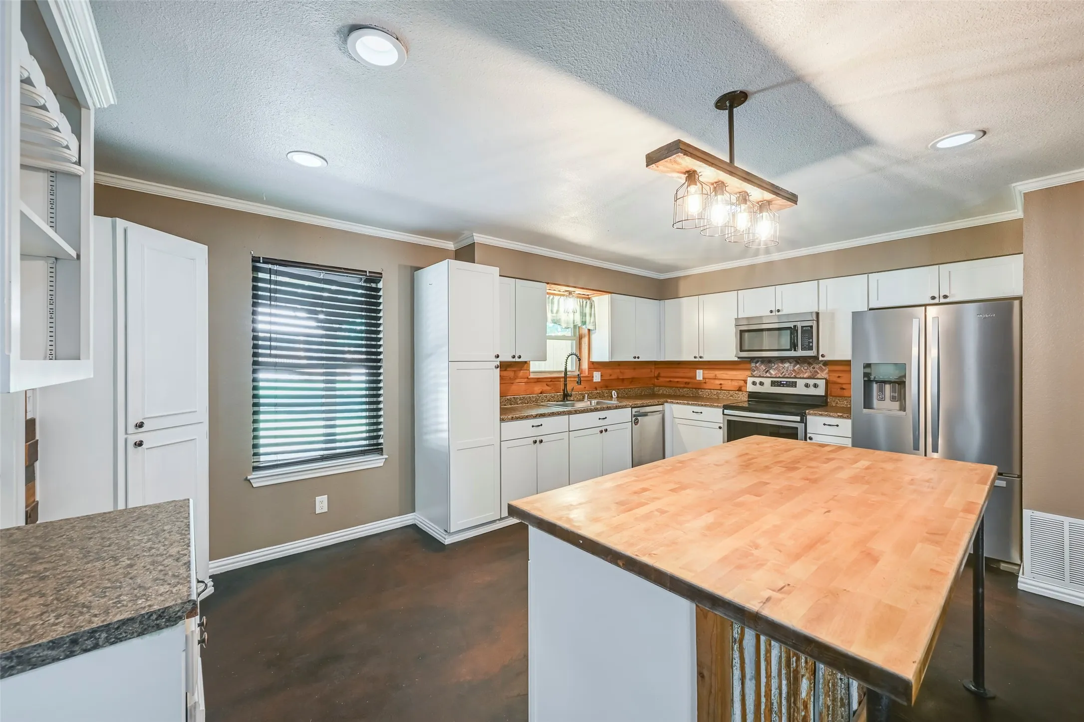 Kitchen featuring a central butcher block island with a corrugated metal base, white cabinetry, stainless steel appliances, a wood-finish backsplash, and recessed lighting