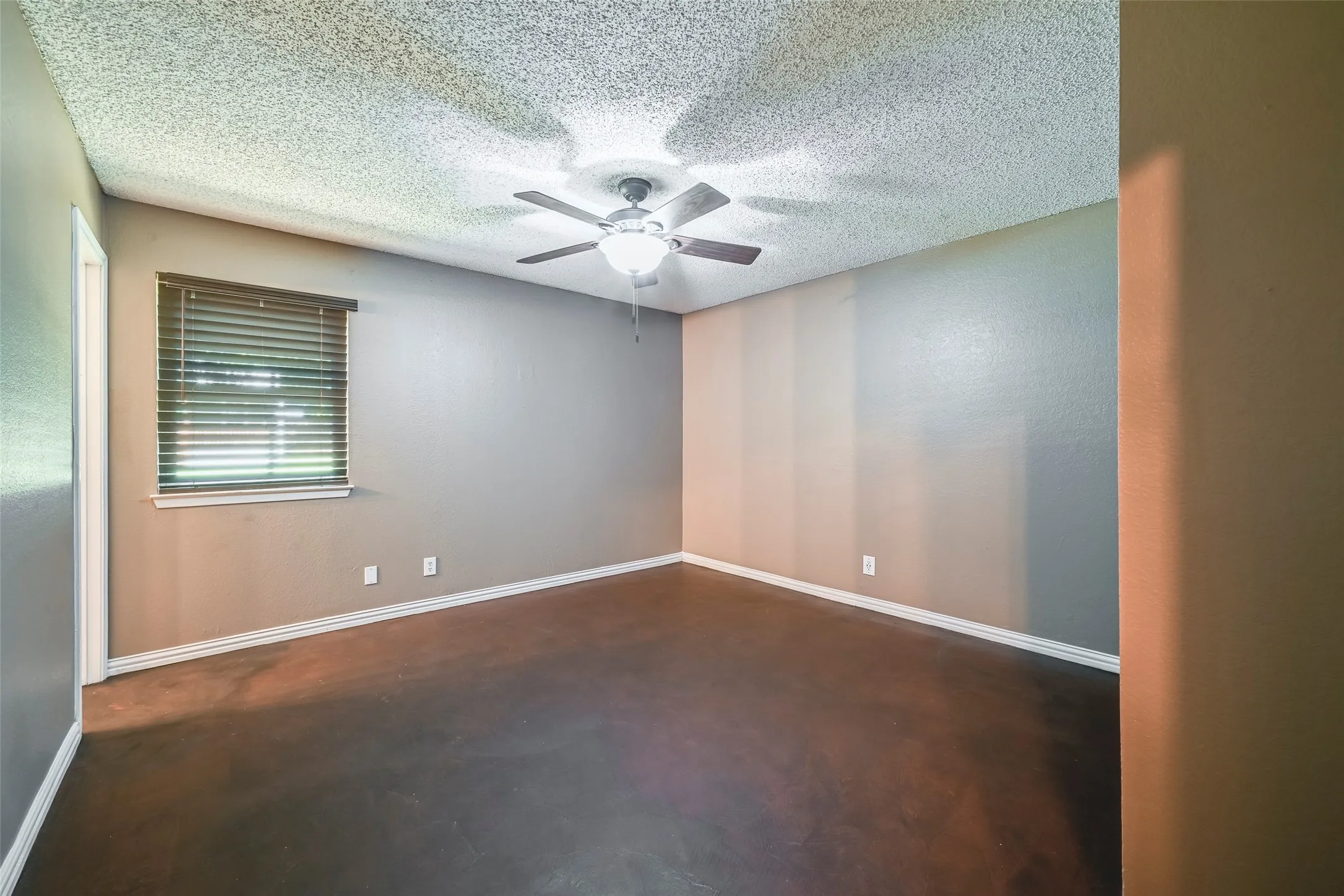 Spacious room featuring dark wood-finish flooring, a ceiling fan with integrated lighting, and neutral-toned walls