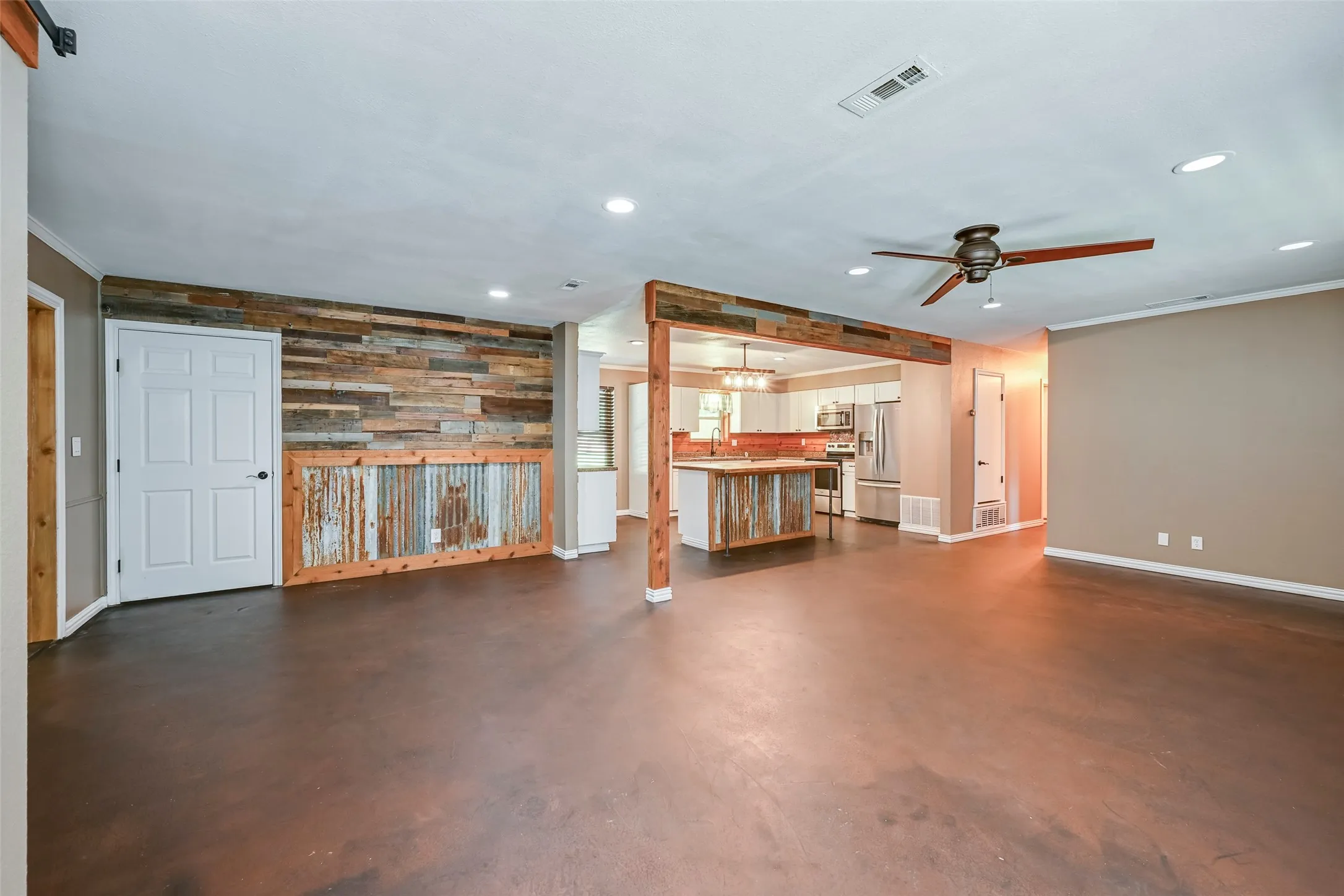 Expansive open-concept living area featuring a rustic wood and corrugated metal accent wall, recessed lighting, and a ceiling fan