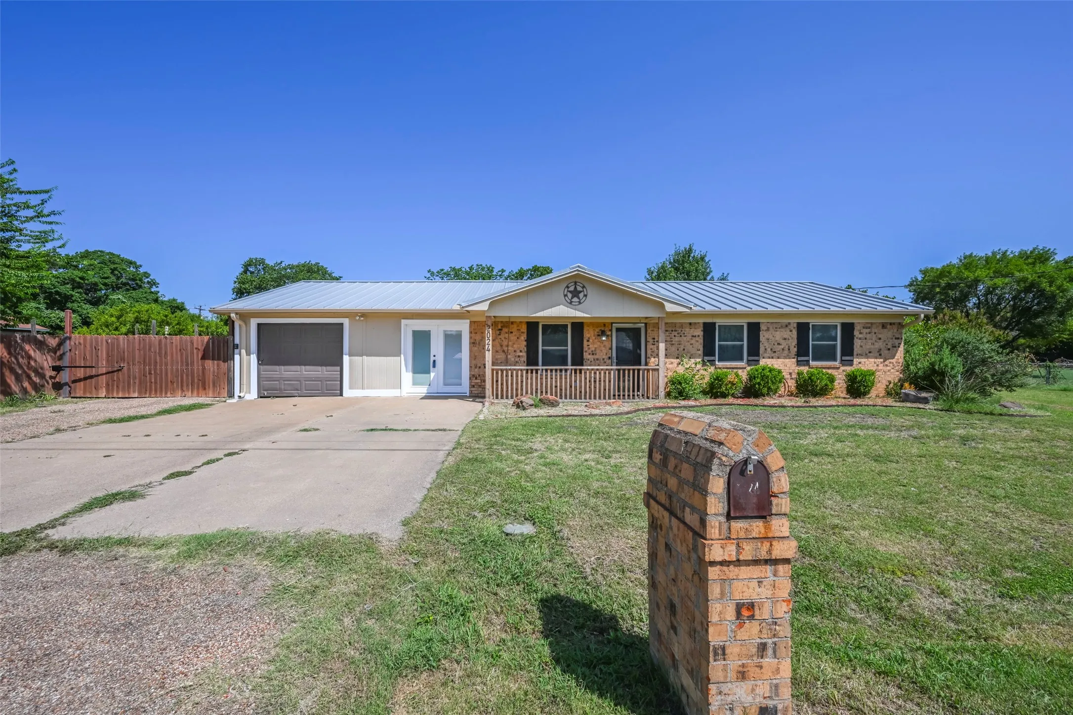 Brick and siding exterior featuring a metal roof, covered front porch, and an attached garage