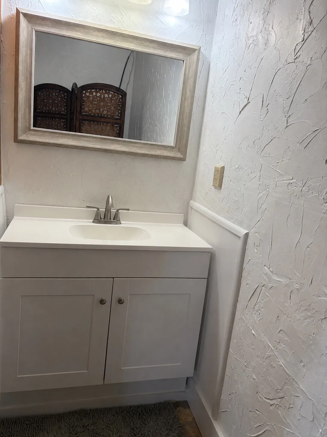 White vanity with an integrated sink and brushed nickel faucet, framed by a distressed-finish mirror