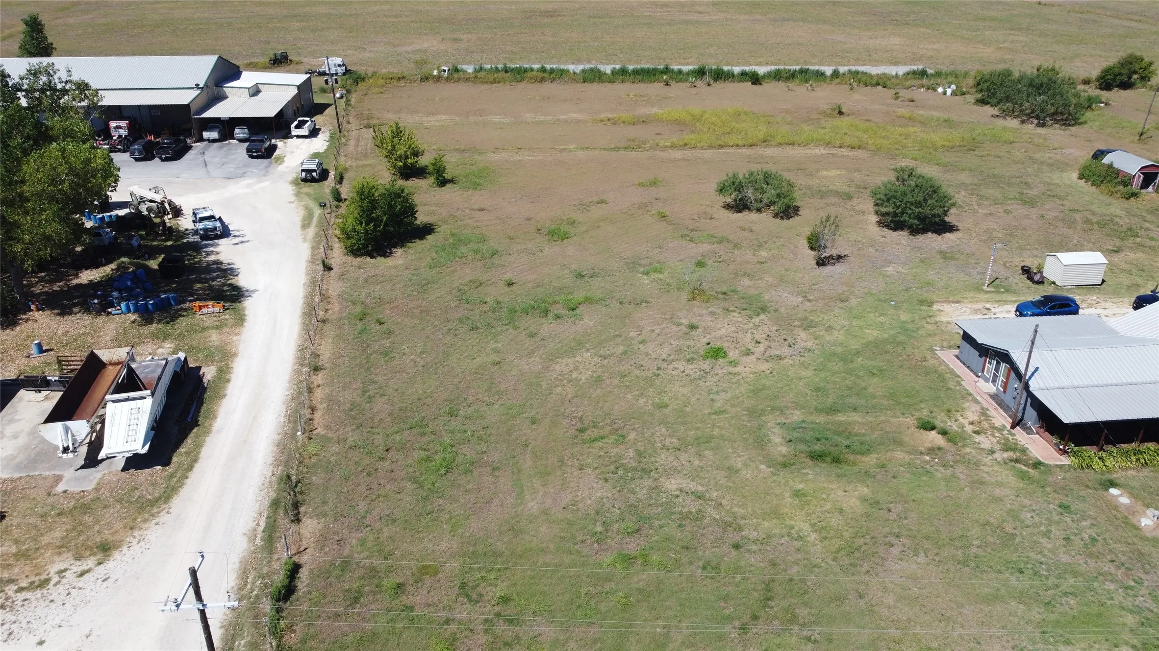 Expansive open land featuring a gravel driveway, a large metal-roofed structure, and a residential-style building with a metal roof