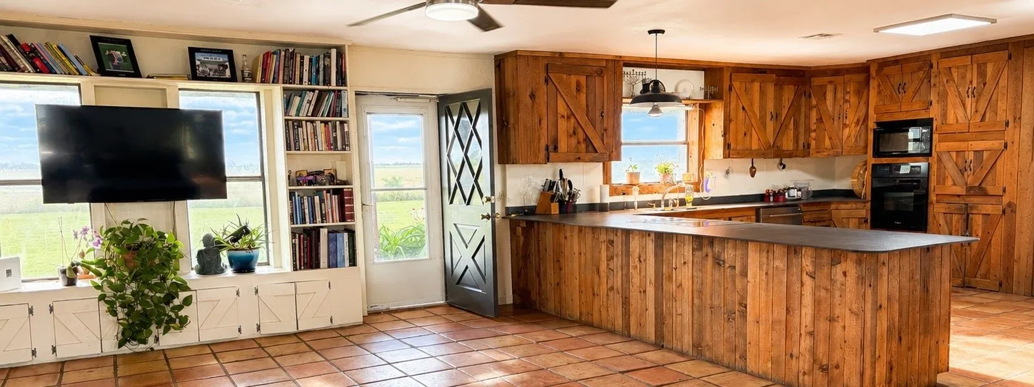 Spacious kitchen and living area featuring terra cotta tile flooring, extensive wood cabinetry, and a large built-in island