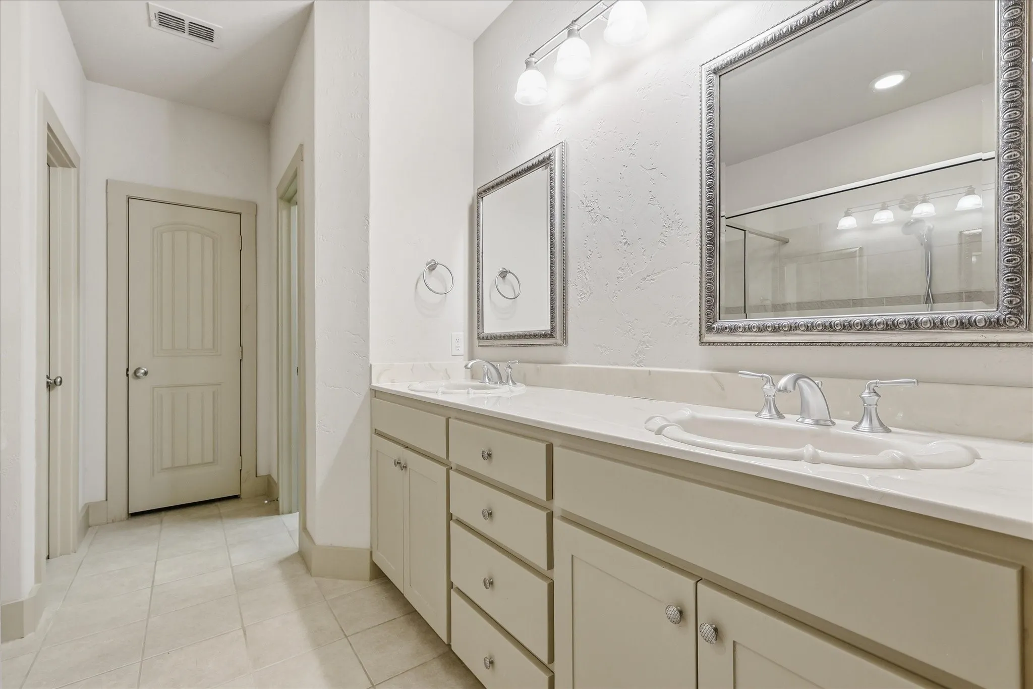 Spacious bathroom featuring a dual vanity with integrated sinks, light-toned countertop, and framed mirrors
