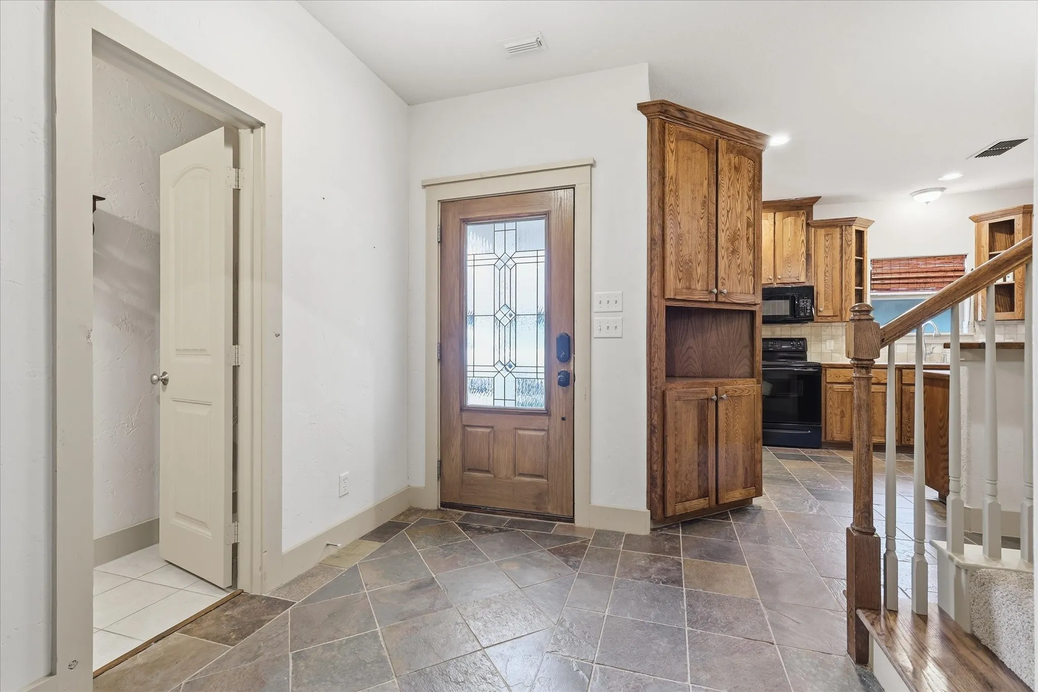 Entryway featuring slate tile flooring, a wood-finish front door with decorative glass, and a built-in wood-finish cabinet