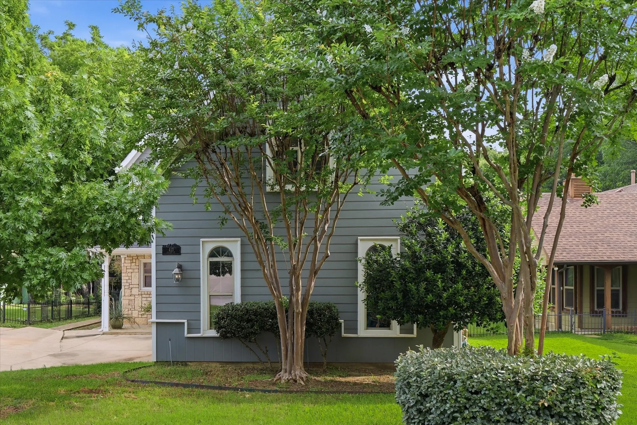 Exterior featuring grey horizontal siding, arched entry doors, white trim, and a manicured lawn