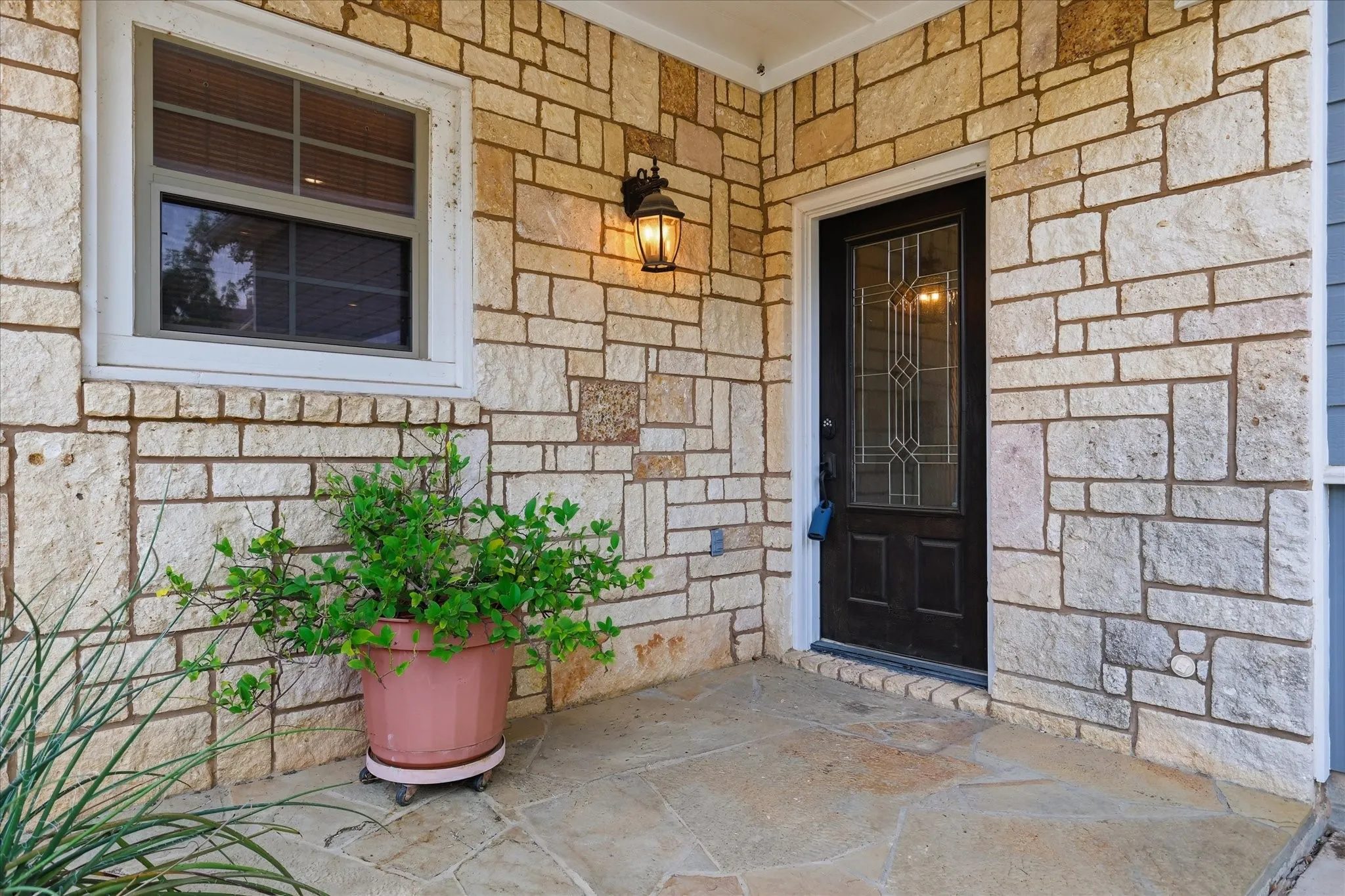 Stone veneer facade featuring a dark entry door with decorative glass, a white-framed window, and a wall-mounted sconce