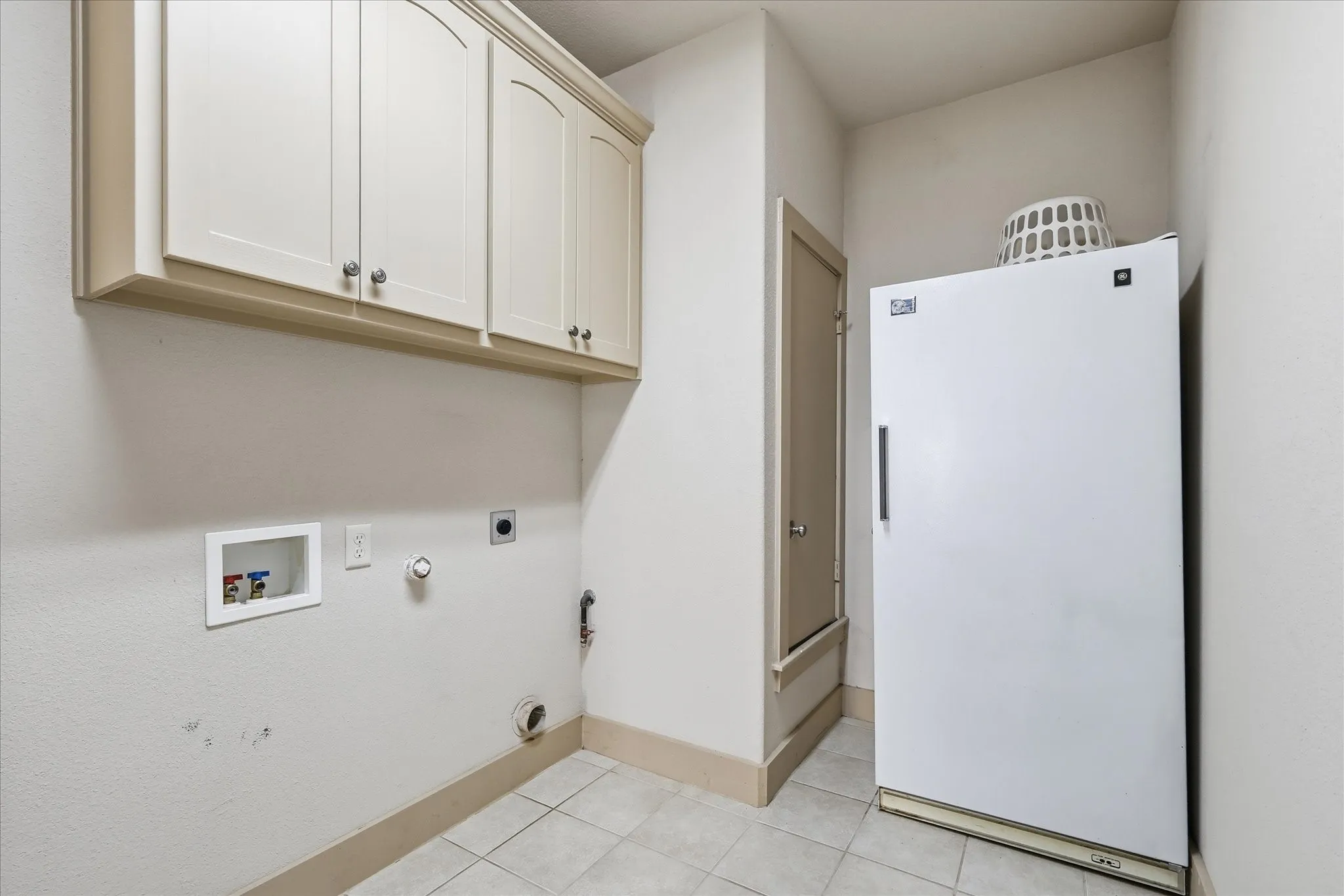 Functional utility area featuring upper cabinetry with arched panel doors, tile flooring, and wall-mounted plumbing connections