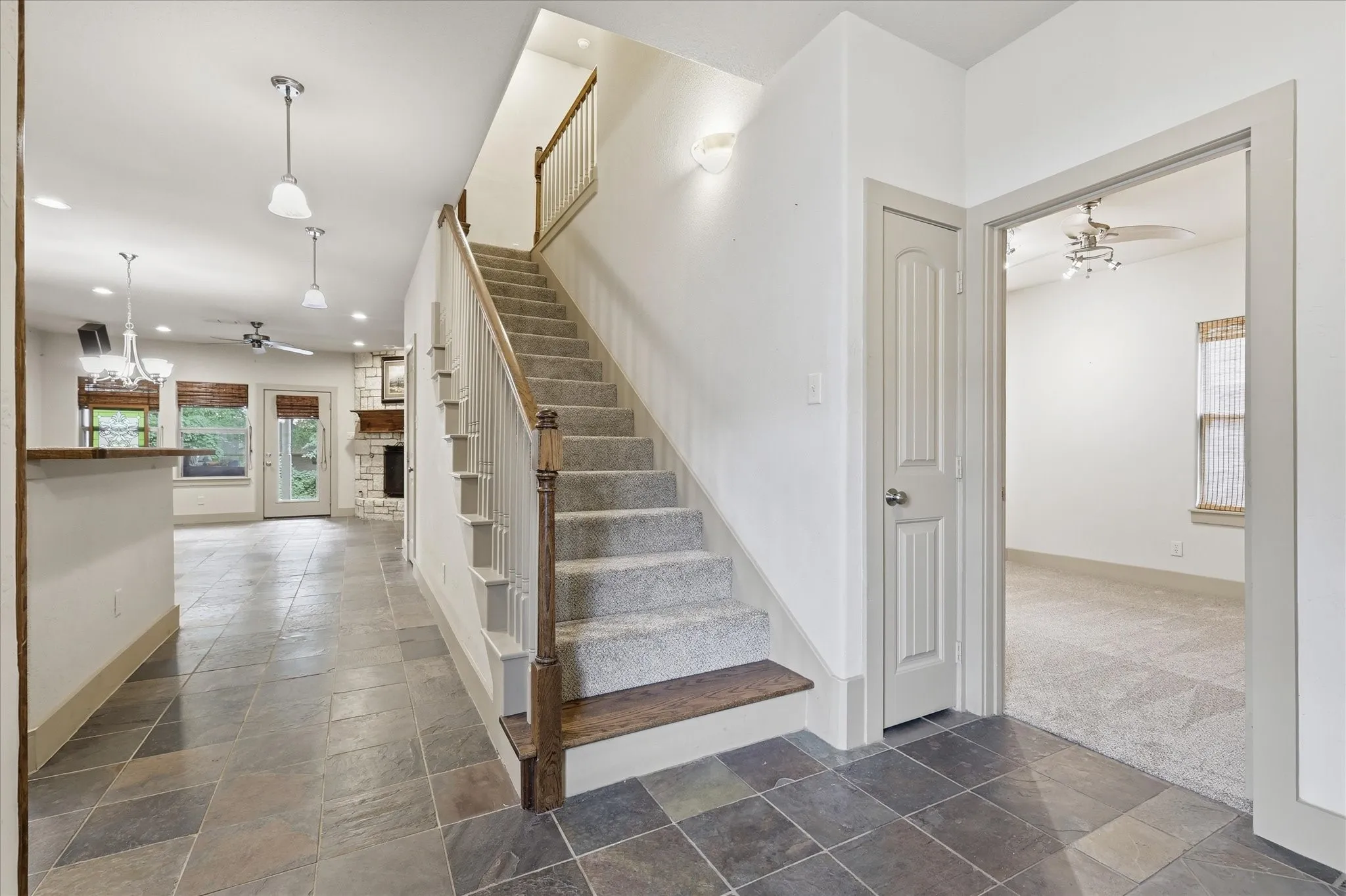 Open concept interior featuring slate tile flooring, a carpeted staircase with wood handrails, and a dedicated room with carpeted flooring