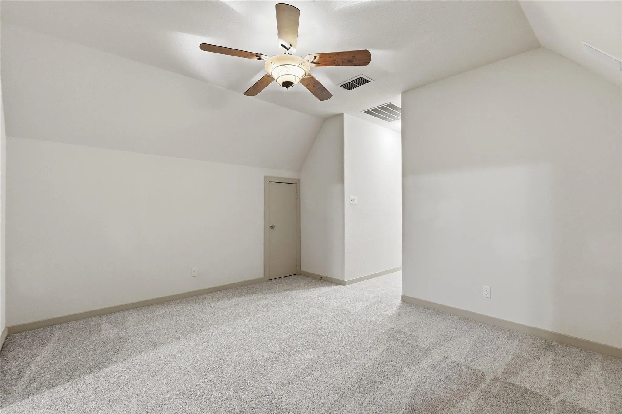 Attic space featuring sloped ceilings, light gray carpeting, and a ceiling fan with wood-finish blades