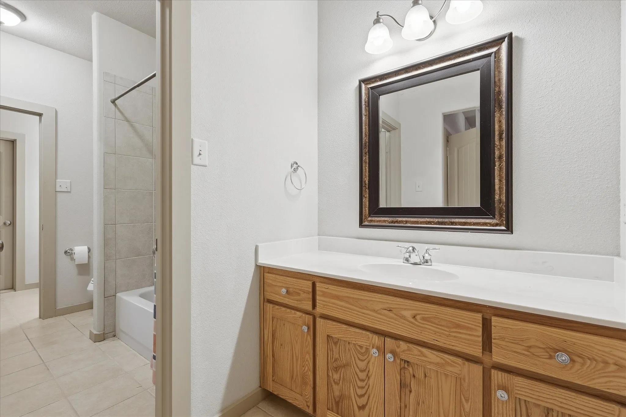 Bathroom featuring a wood-finish vanity with a white countertop, an undermount sink, a framed mirror, and a three-light fixture
