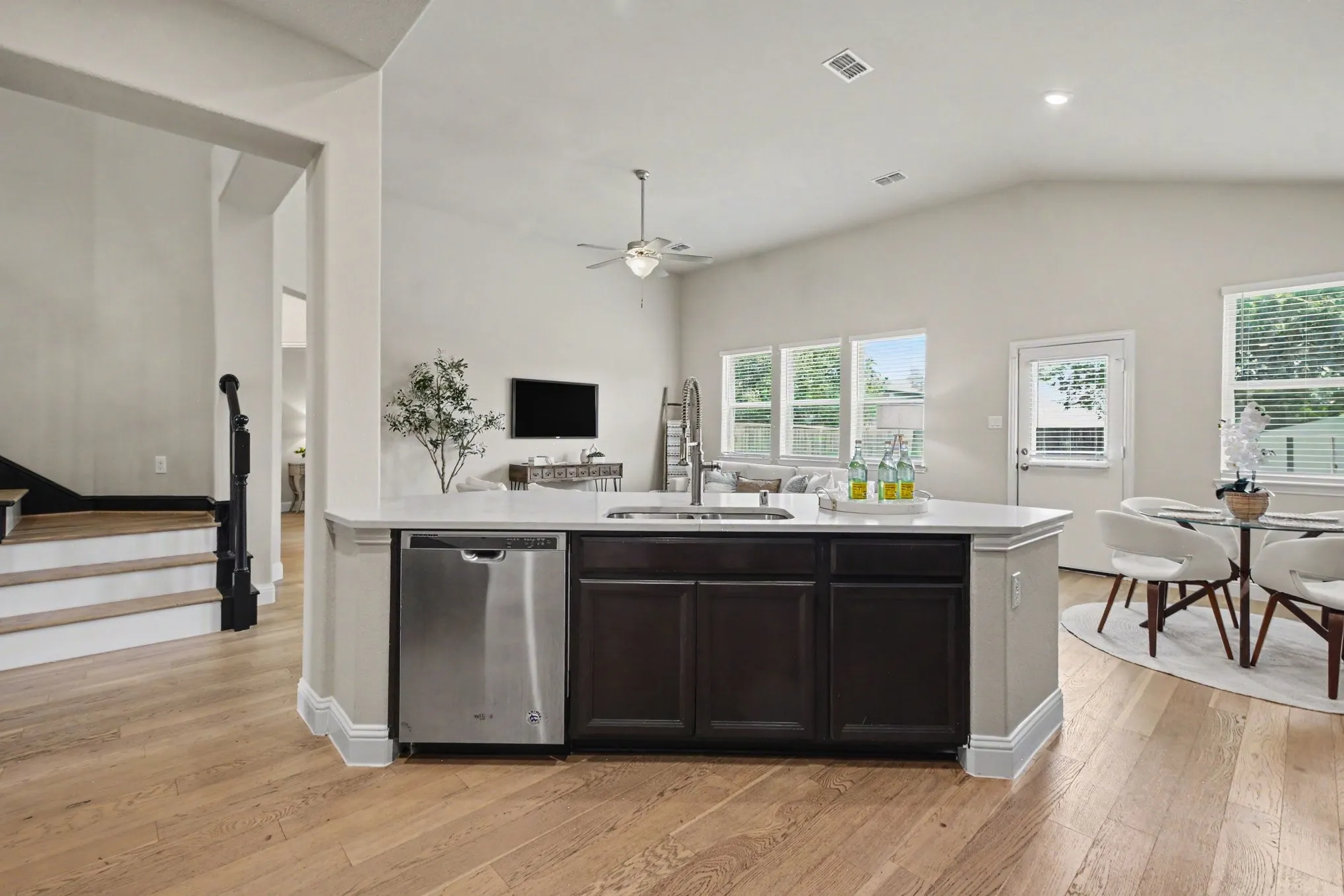 Kitchen island with stone countertop, stainless steel dishwasher, wood-finish flooring, and vaulted ceiling