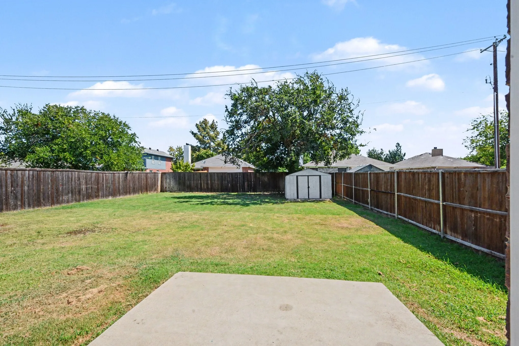 Expansive backyard featuring a wood fence, mature trees, a storage shed, and a concrete patio