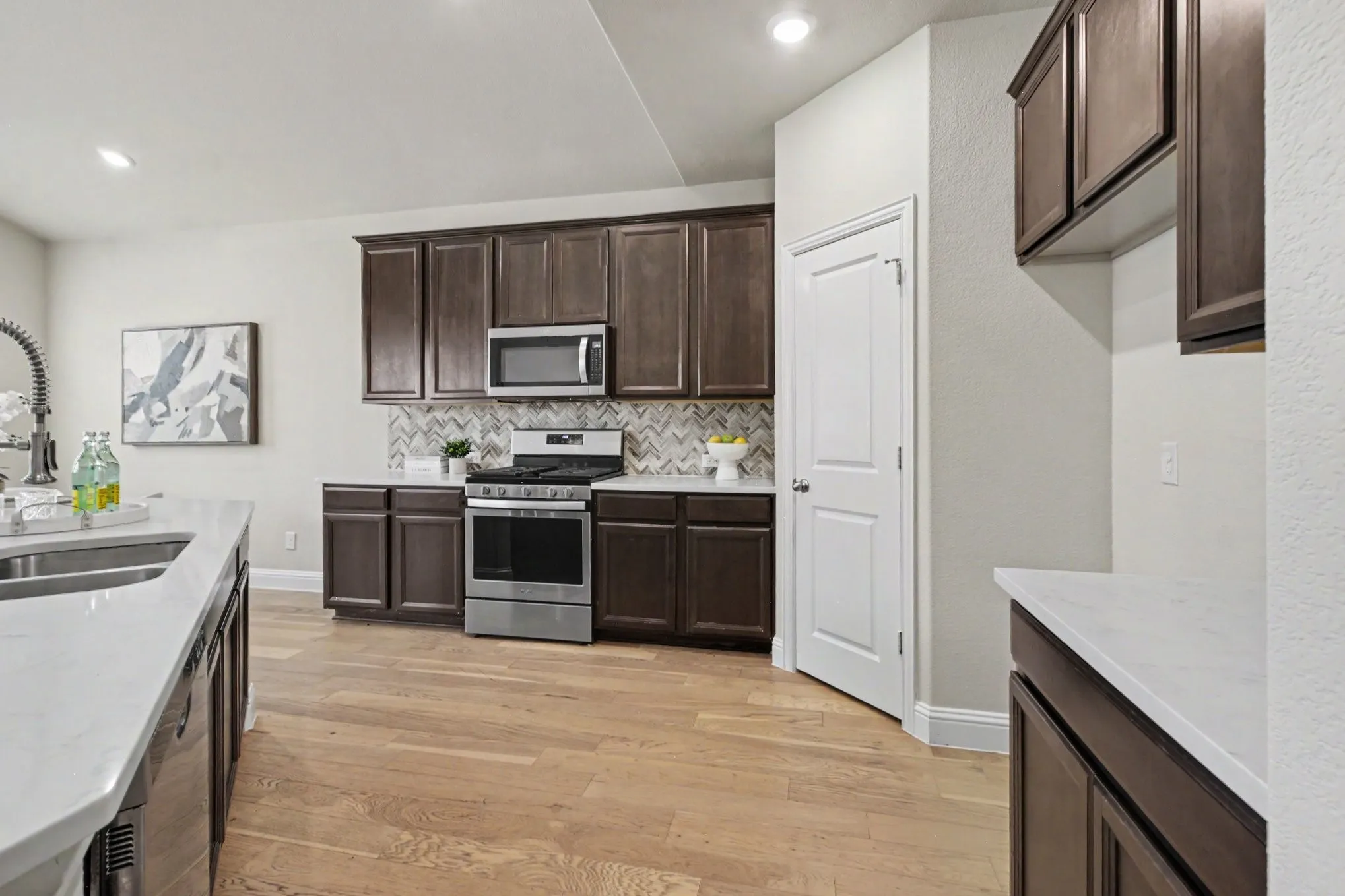 Kitchen featuring wood-finish flooring, dark wood cabinetry, white countertops, and a tile backsplash
