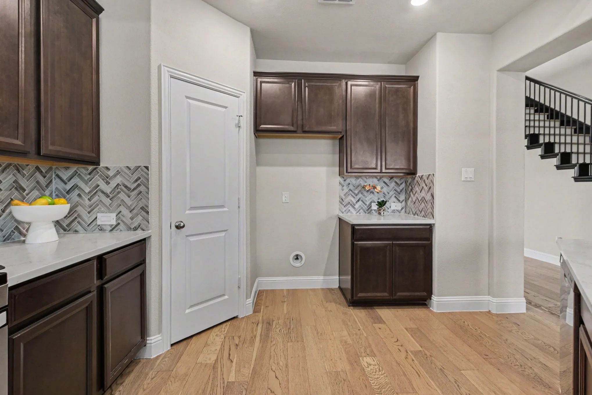 Wood-finish flooring with dark wood cabinetry, light countertops, and a chevron tile backsplash