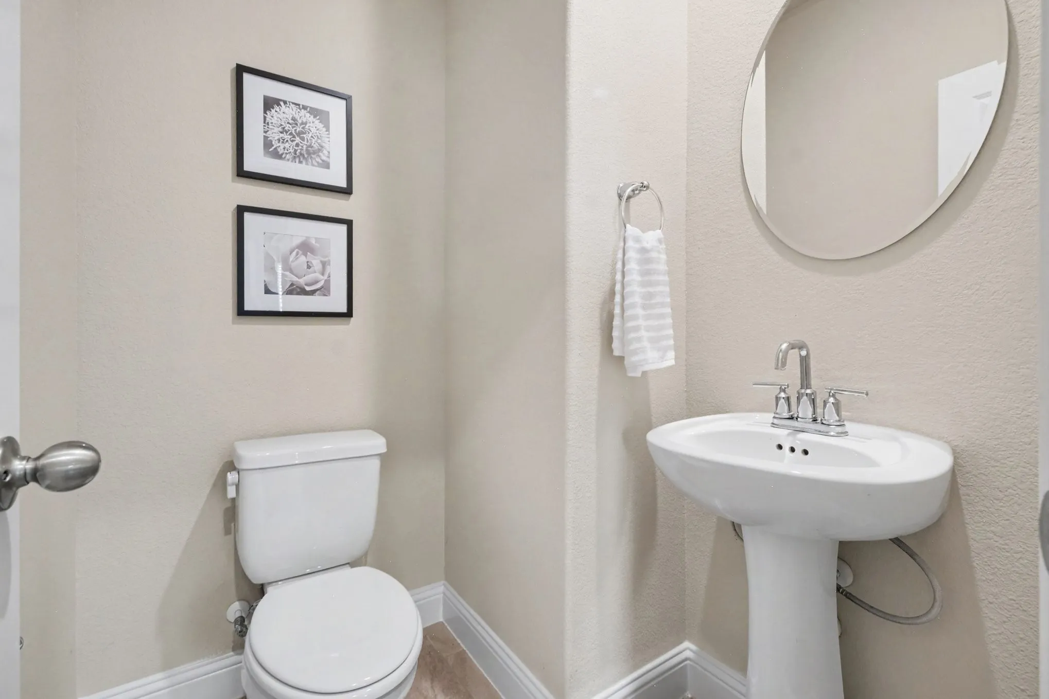 Pedestal sink with chrome faucet, oval wall-mounted mirror, and white toilet