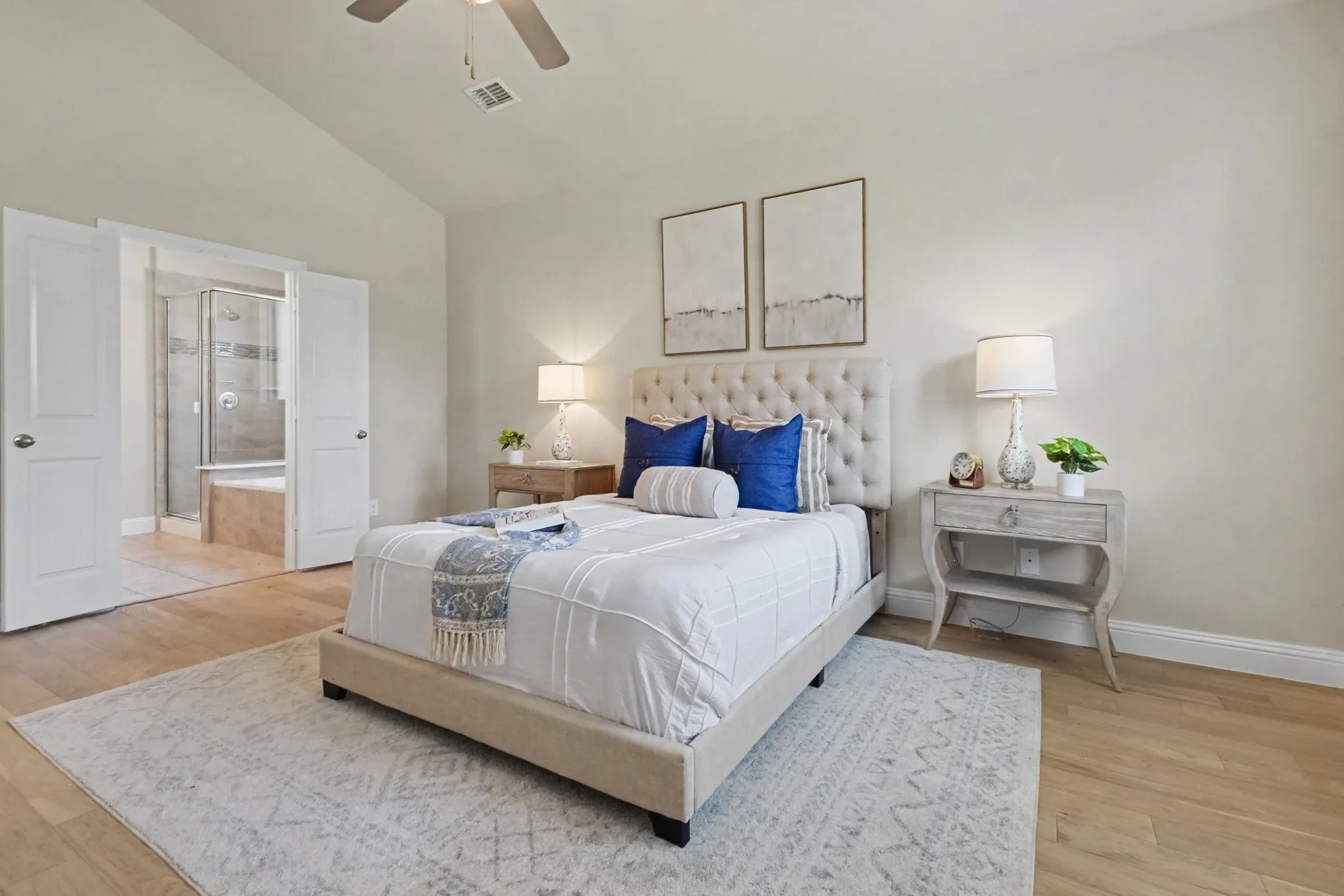 Vaulted ceiling with a ceiling fan, light wood-finish flooring, and double doors opening to a bathroom featuring a shower and built-in tub