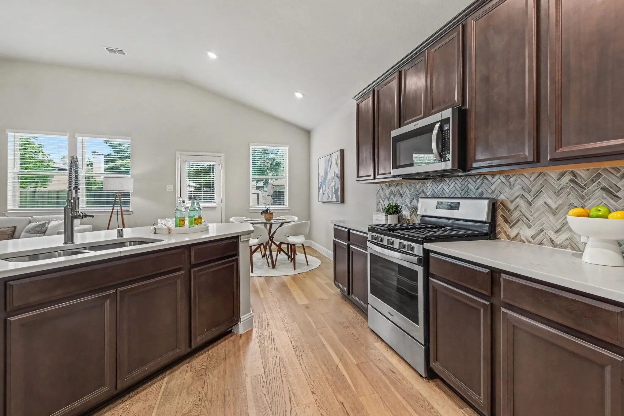 Vaulted ceiling with recessed lighting, wood-finish flooring, dark wood cabinetry, white countertops, and stainless steel appliances