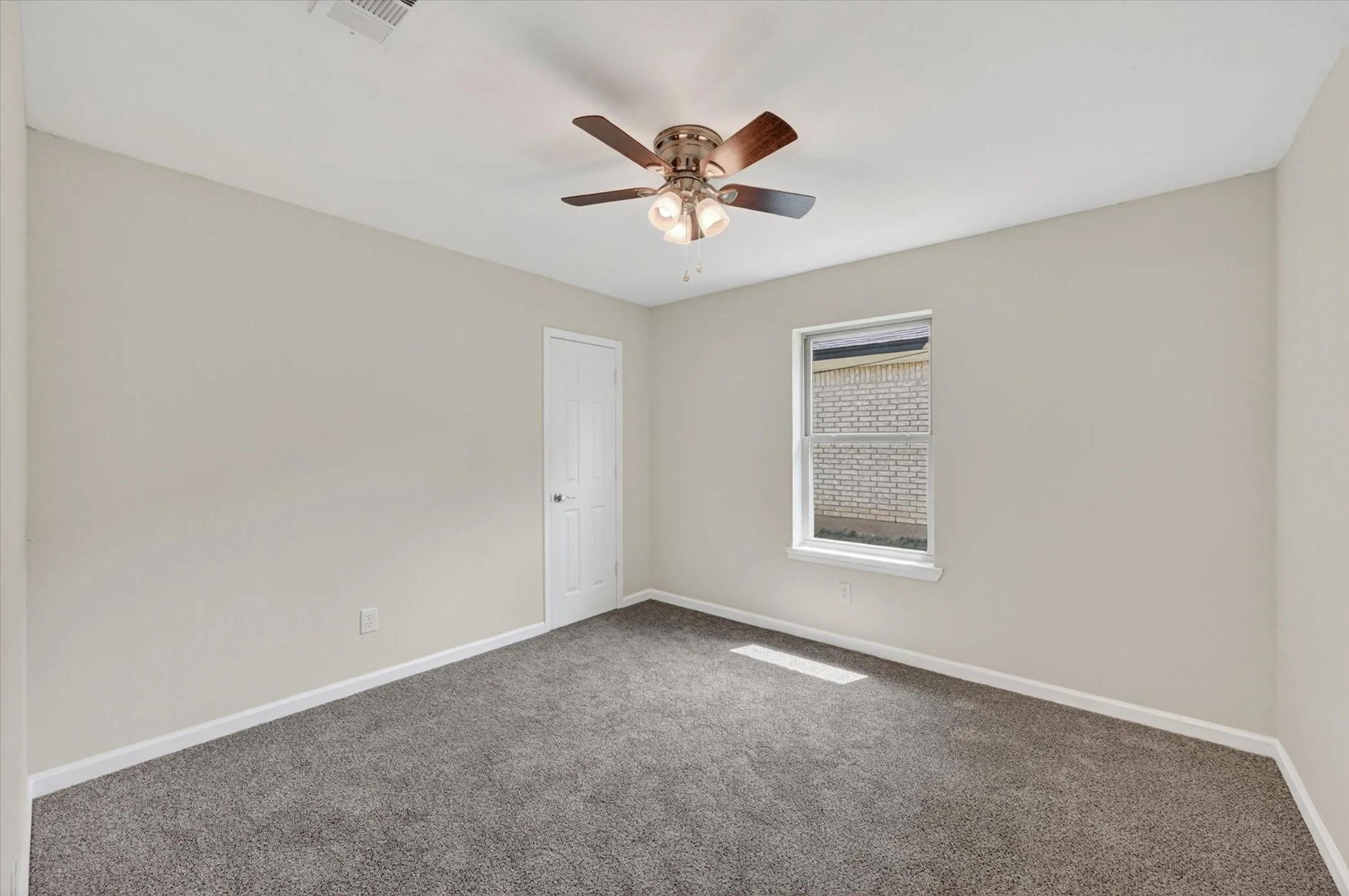 Carpeted room featuring a ceiling fan with integrated lighting, a window, and a white interior door