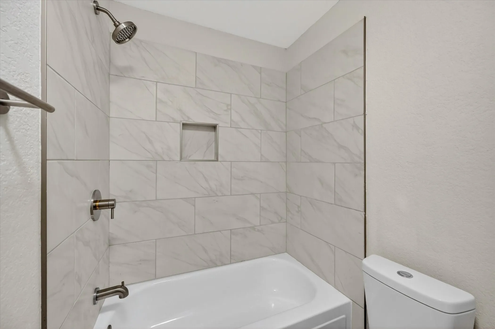 Bathtub with subway tile surround featuring a recessed niche and brushed nickel shower fixtures