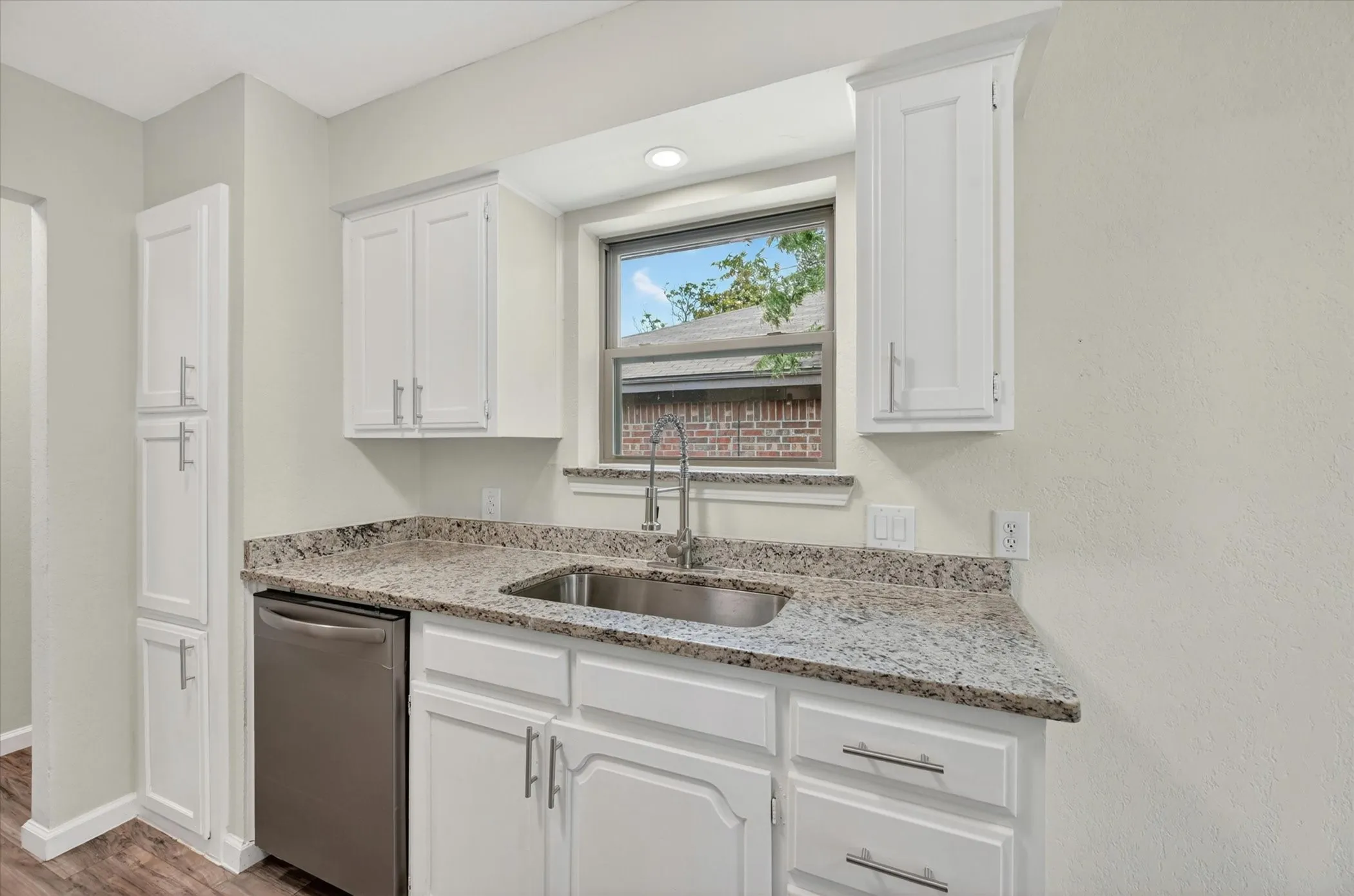 Kitchen area featuring white cabinetry with silver hardware, granite countertops, a stainless steel sink with a gooseneck faucet, and stainless steel dishwasher