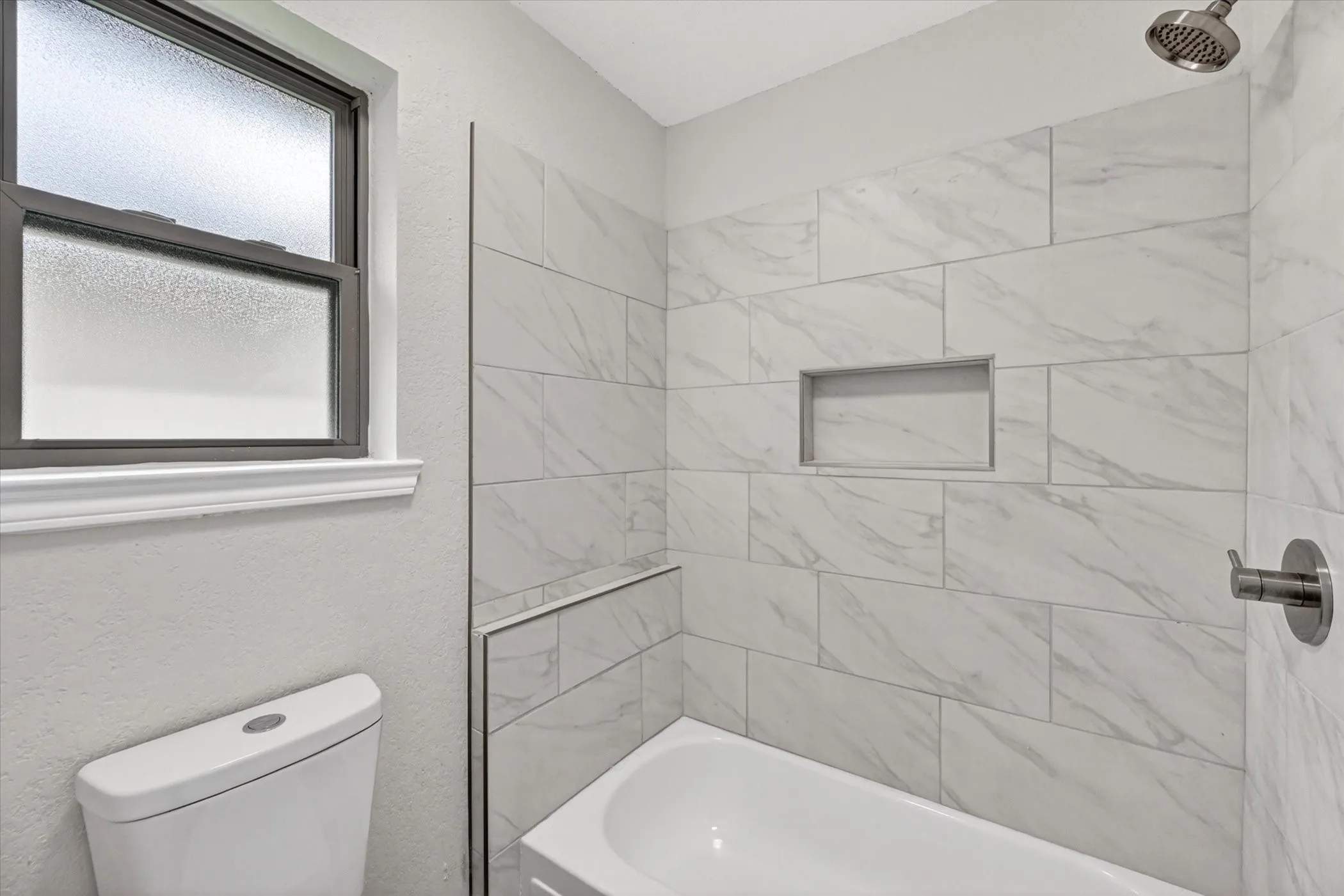Bathtub with white subway tile surround, featuring a recessed niche and brushed nickel shower fixtures