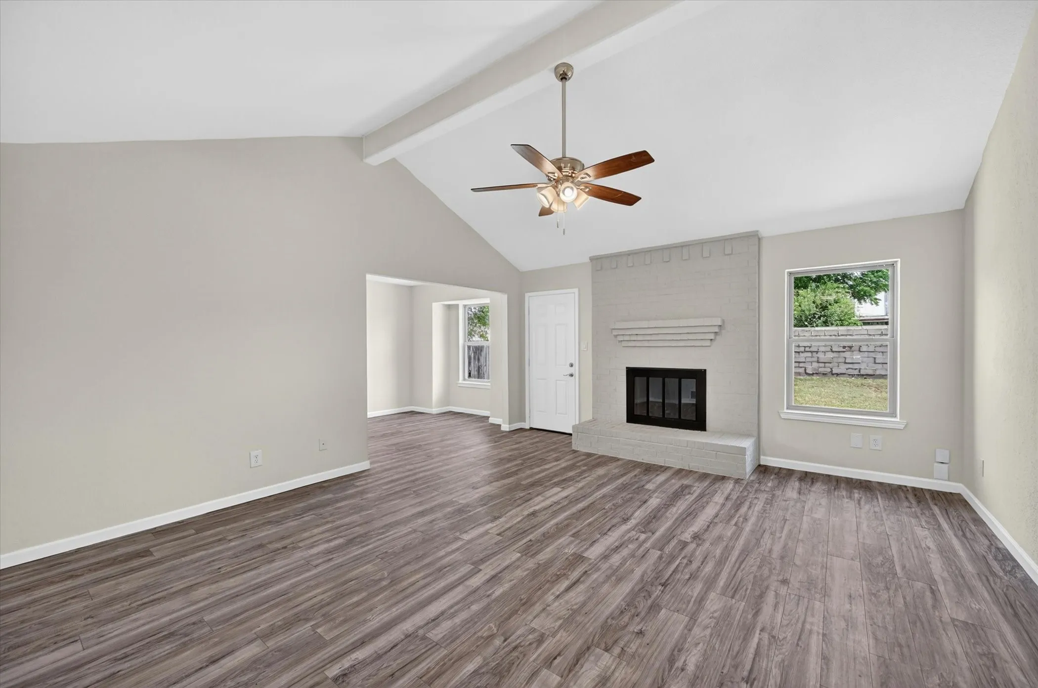 Spacious living area featuring vaulted ceilings, wood-finish flooring, and a painted brick fireplace with a mantel