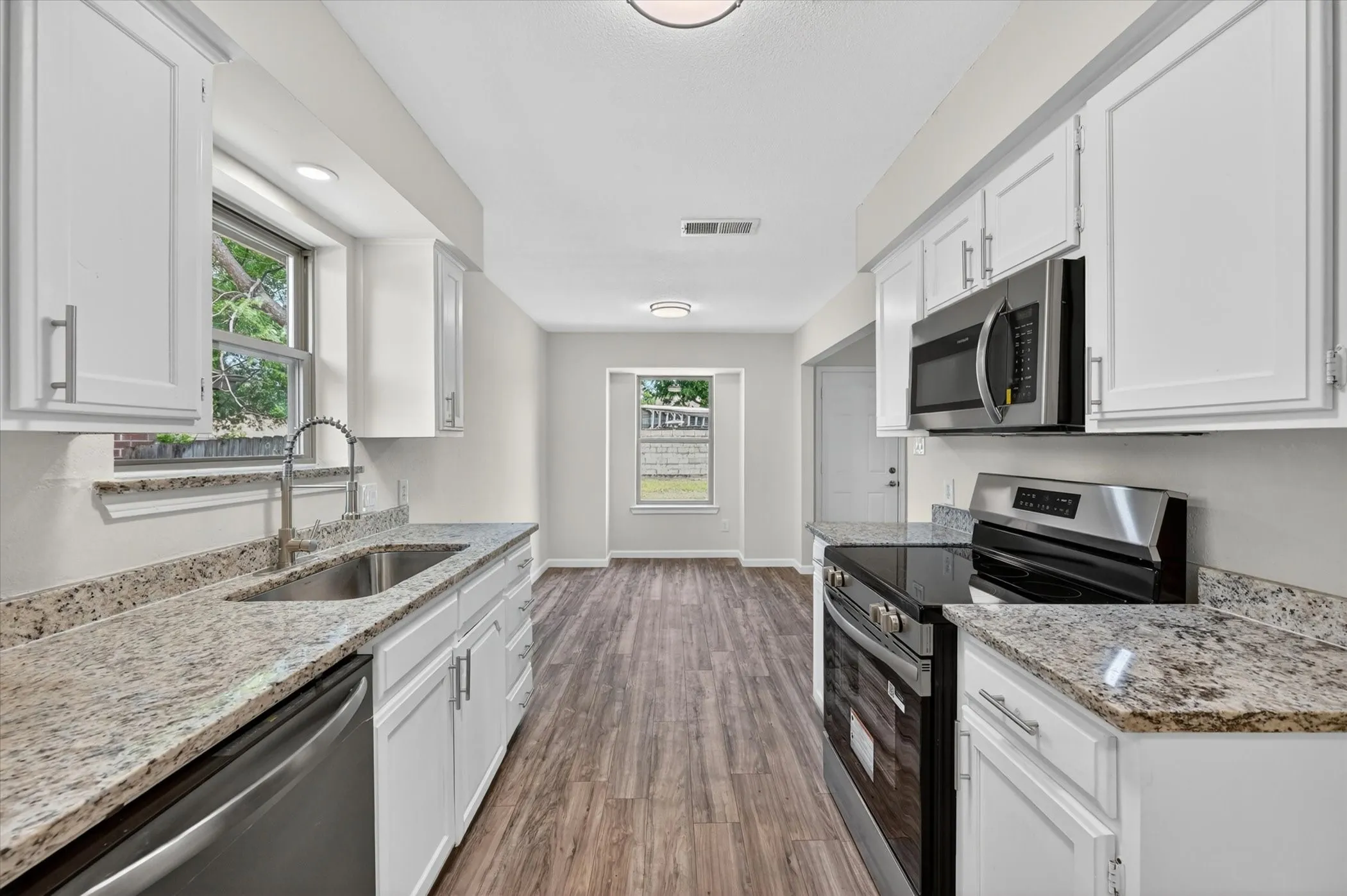 Galley kitchen featuring white cabinetry, stone-finish countertops, stainless steel appliances, a double basin sink, and wood-finish flooring