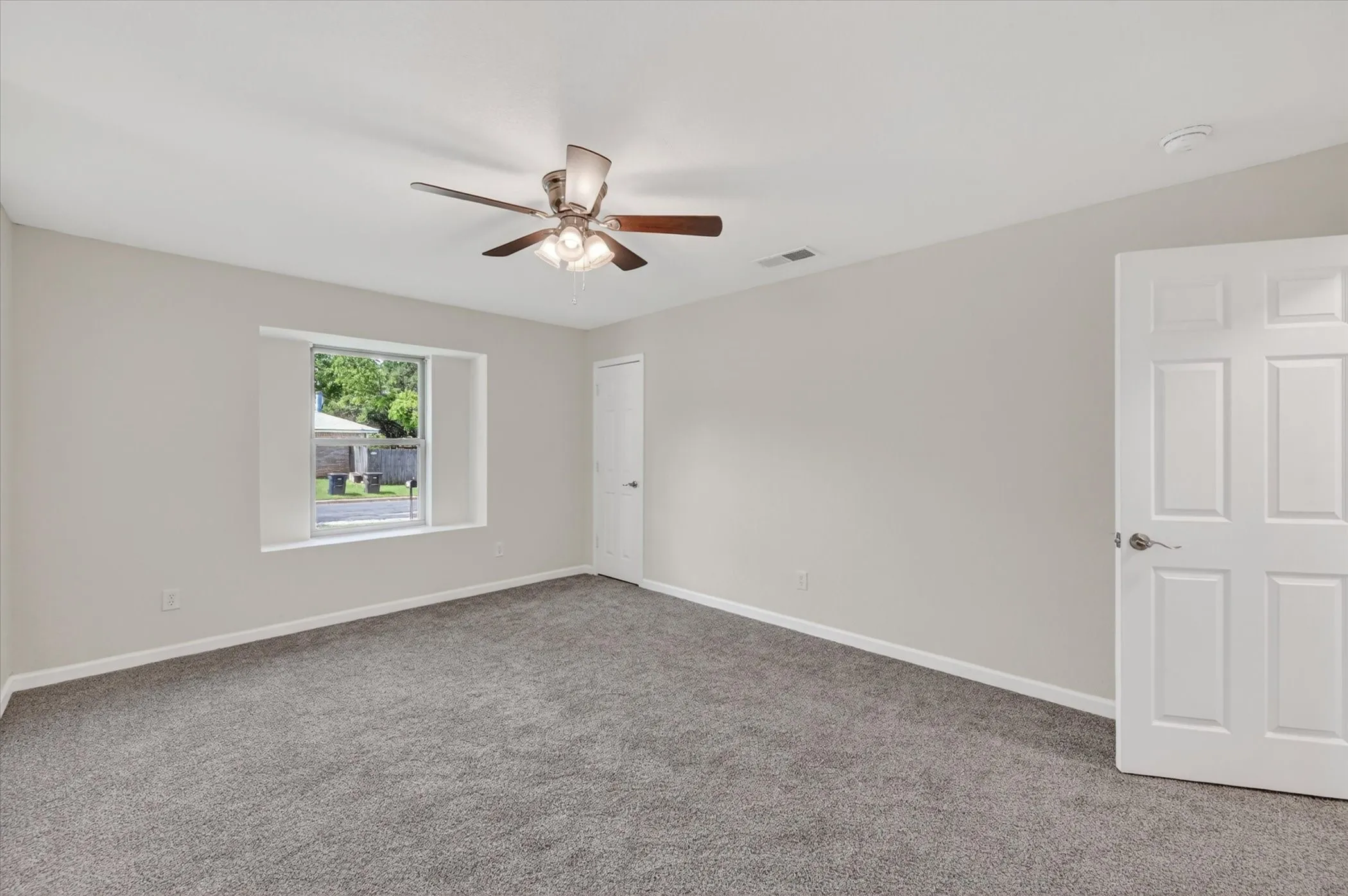 Spacious room featuring neutral grey wall paint, plush grey carpeting, a multi-speed ceiling fan with integrated lighting, and a white six-panel door