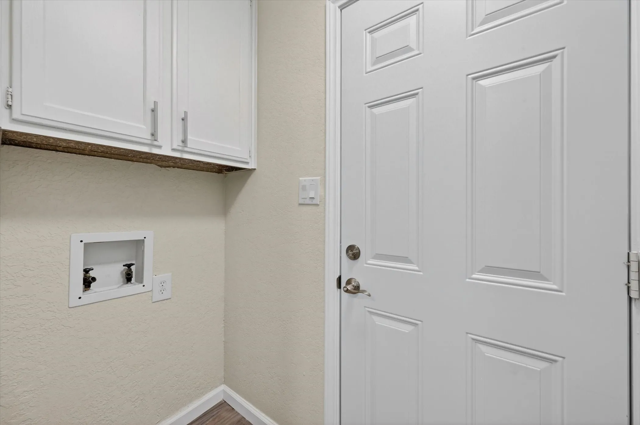Utility area featuring a paneled door, built-in upper cabinetry with brushed nickel hardware, a laundry hookup station, and wood-finish flooring