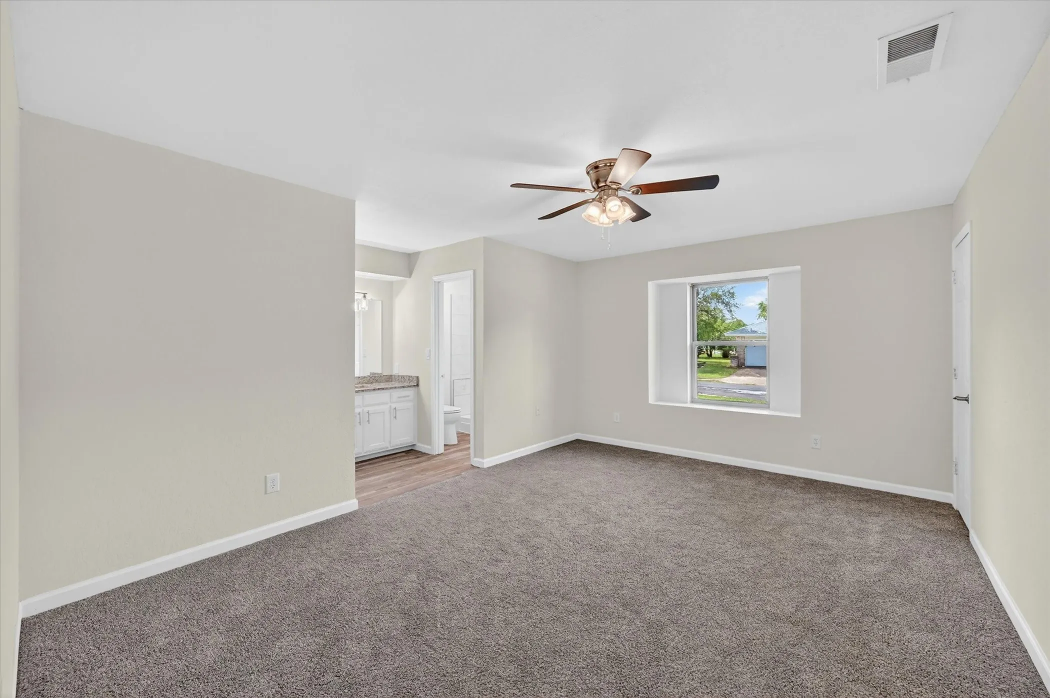 Spacious room featuring neutral paint, gray carpet, and a ceiling fan with light fixture