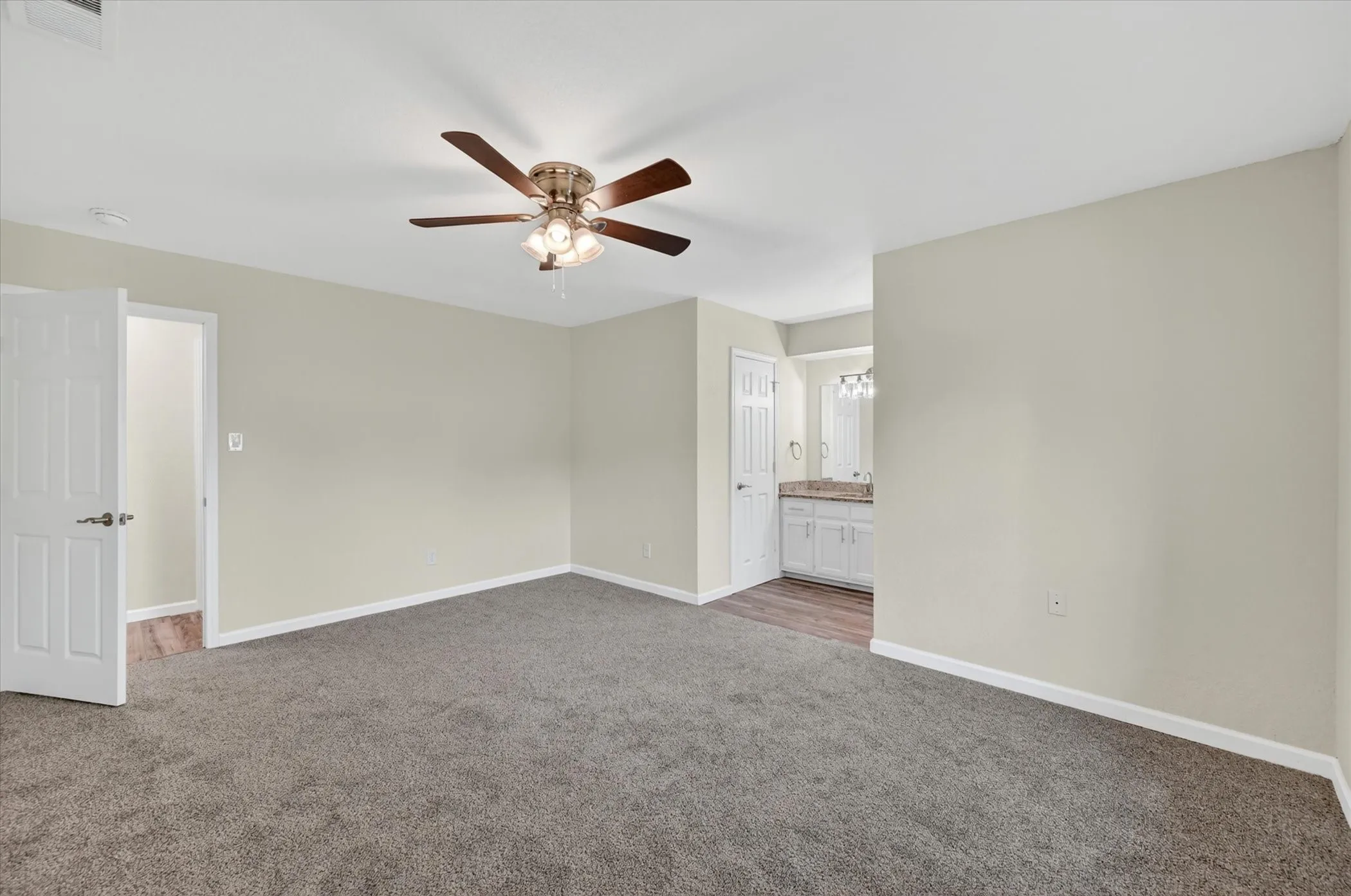 Spacious interior room featuring plush gray carpeting, light neutral wall tones, and a ceiling fan with integrated lighting