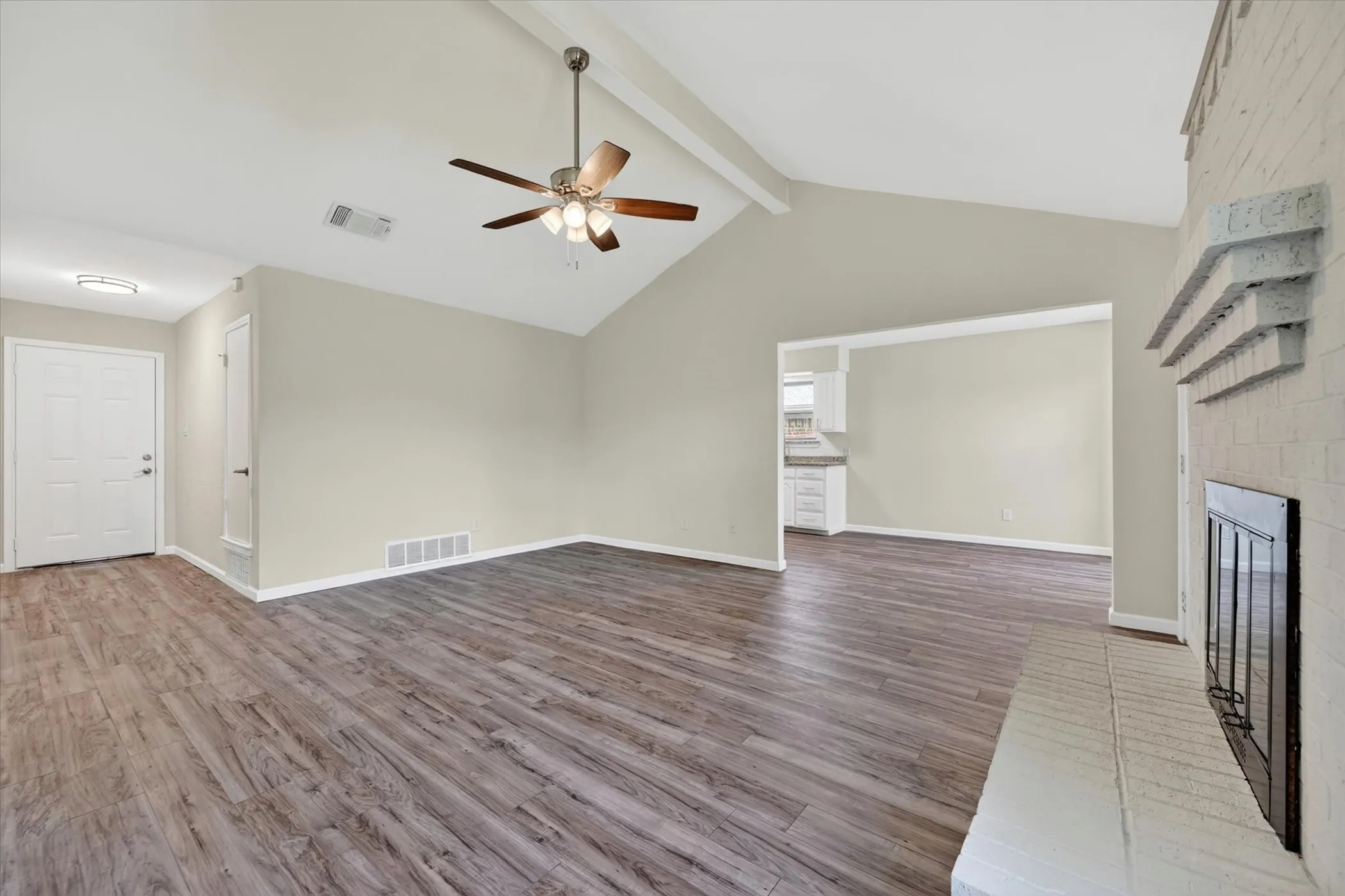 Spacious living area featuring vaulted ceilings, wood-finish flooring, a ceiling fan, and a painted brick fireplace