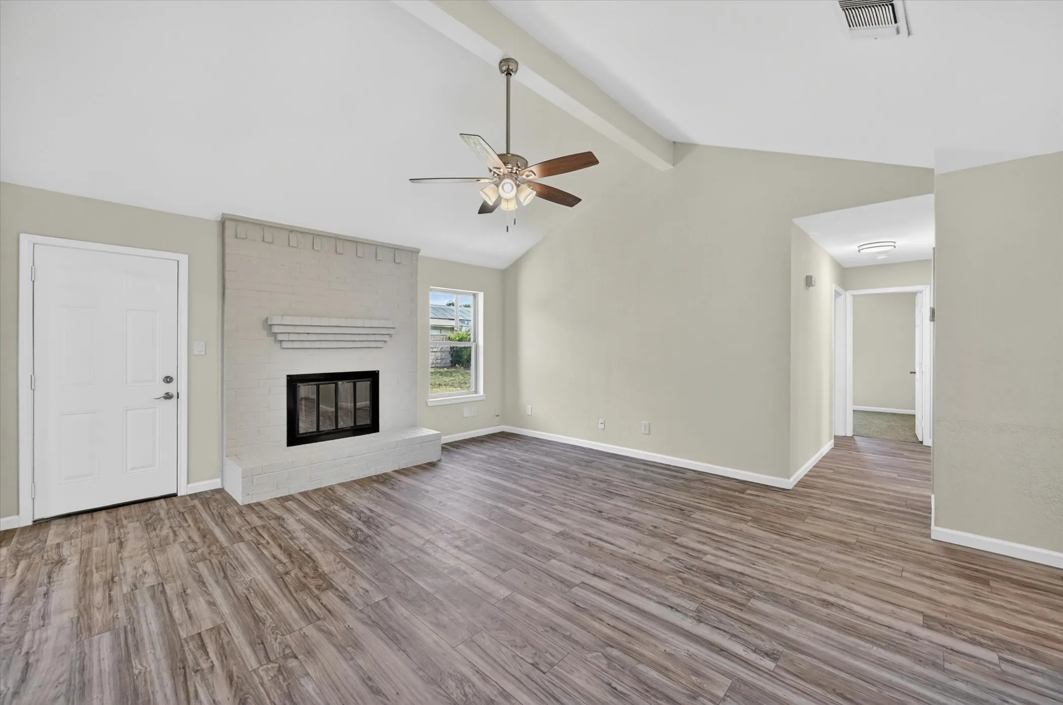 Spacious room featuring vaulted ceilings, wood-finish flooring, and a brick fireplace