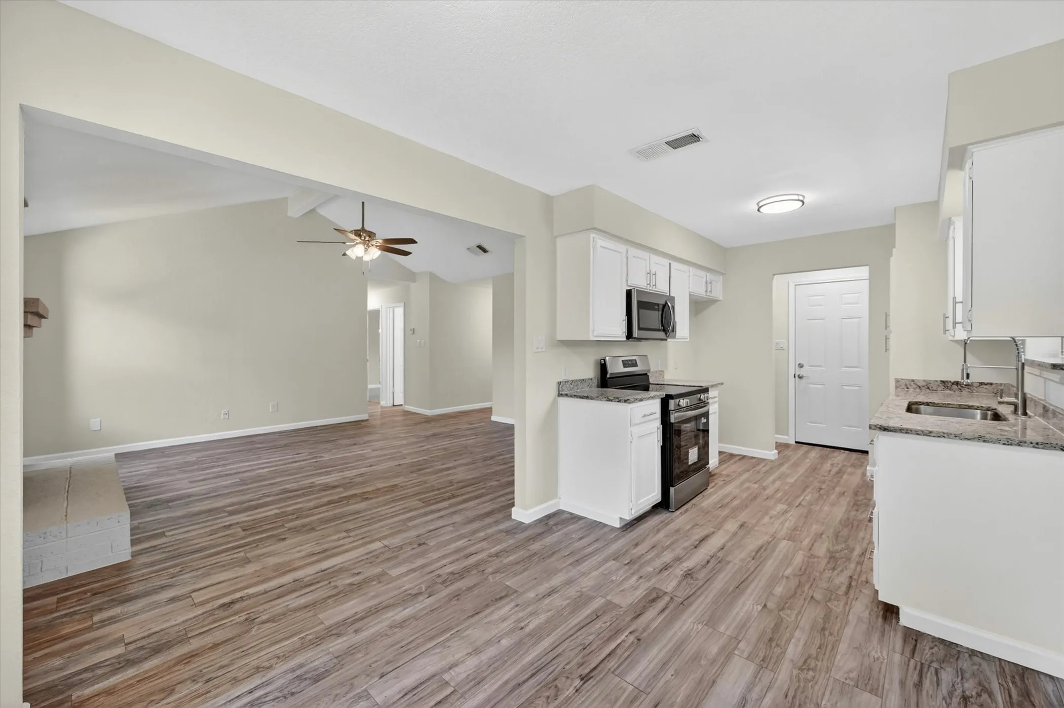 Open-concept kitchen featuring white cabinetry, stainless steel appliances, and wood-finish flooring