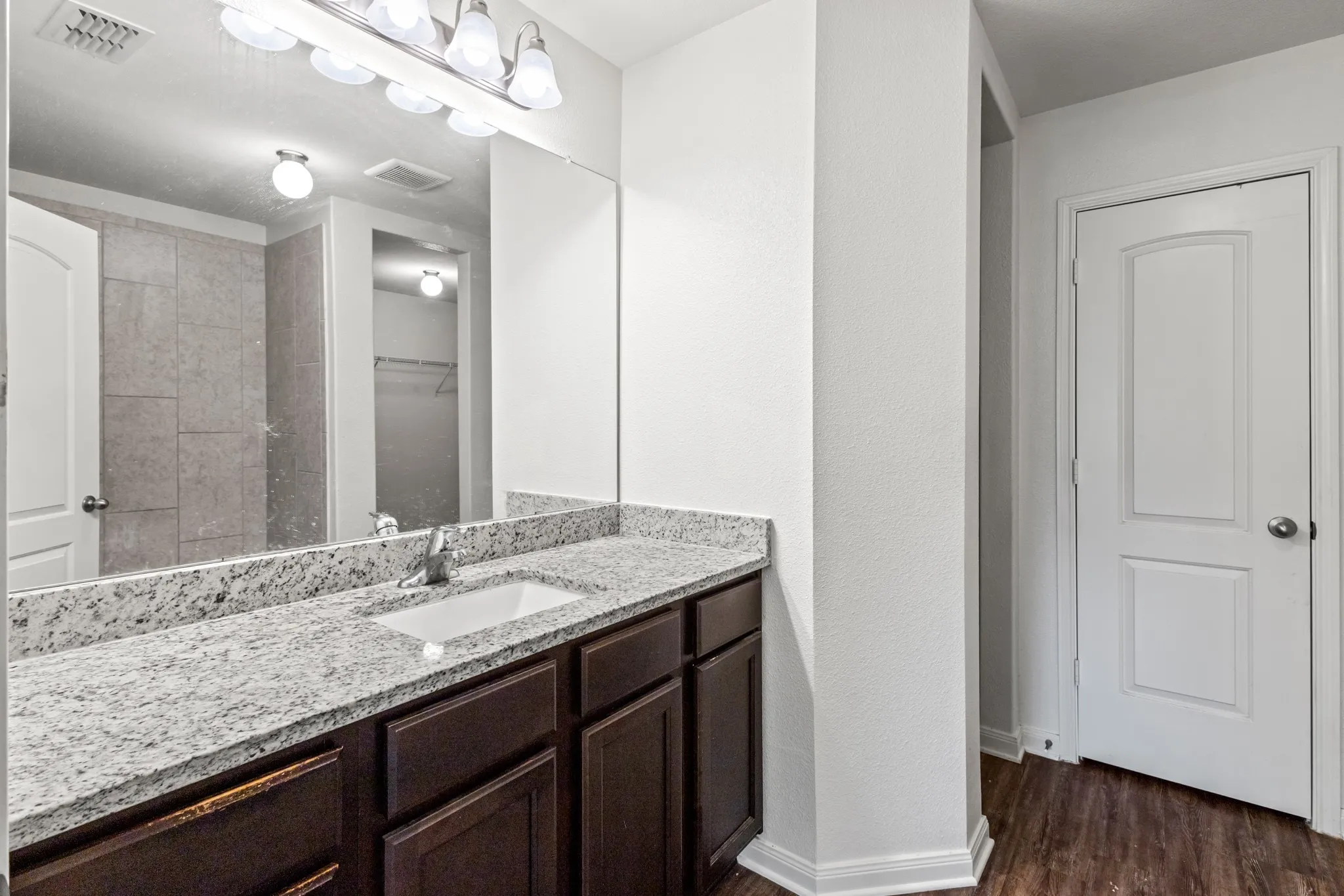 Bathroom vanity featuring a light-toned countertop, under-mount sink, dark wood-finish cabinetry, and a wide mirror