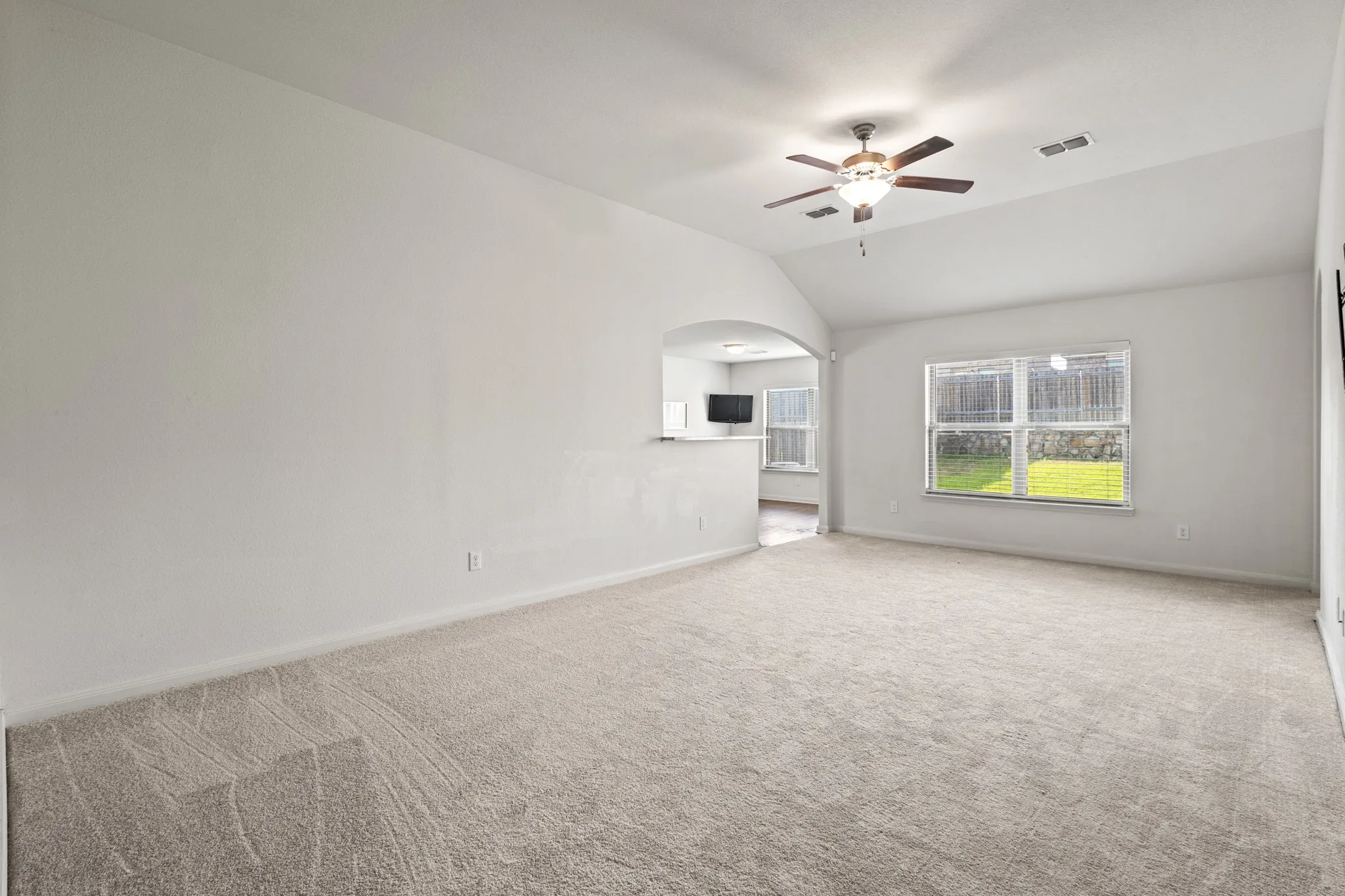 Spacious living area featuring light-colored carpet flooring, a vaulted ceiling, and a ceiling fan with integrated lighting