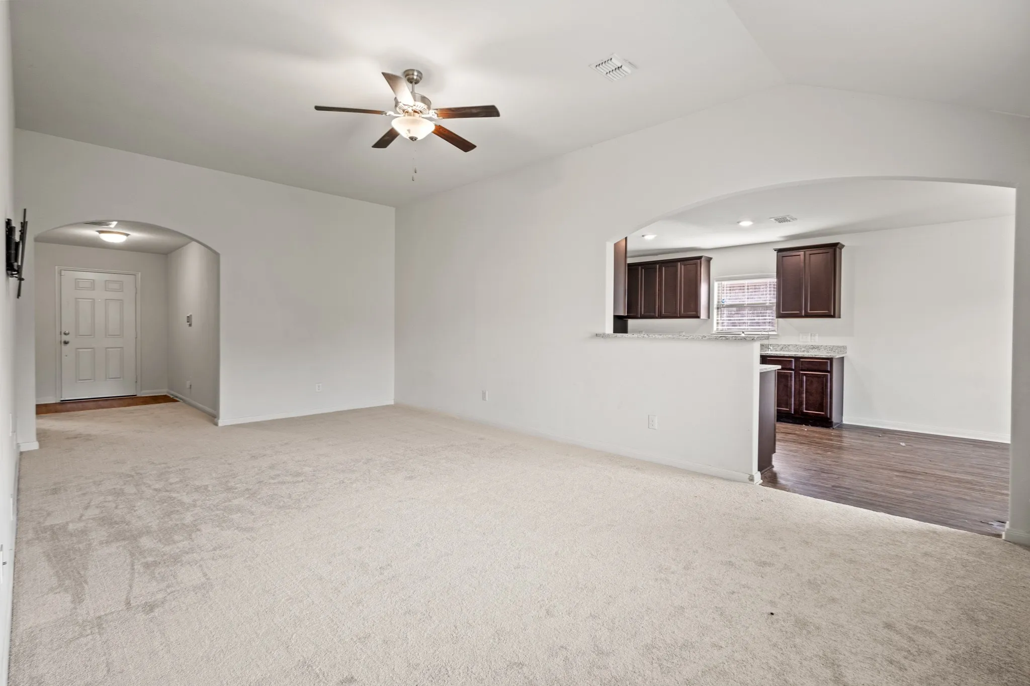 Carpeted living area featuring an arched entry, a ceiling fan, and a pass-through opening to the kitchen