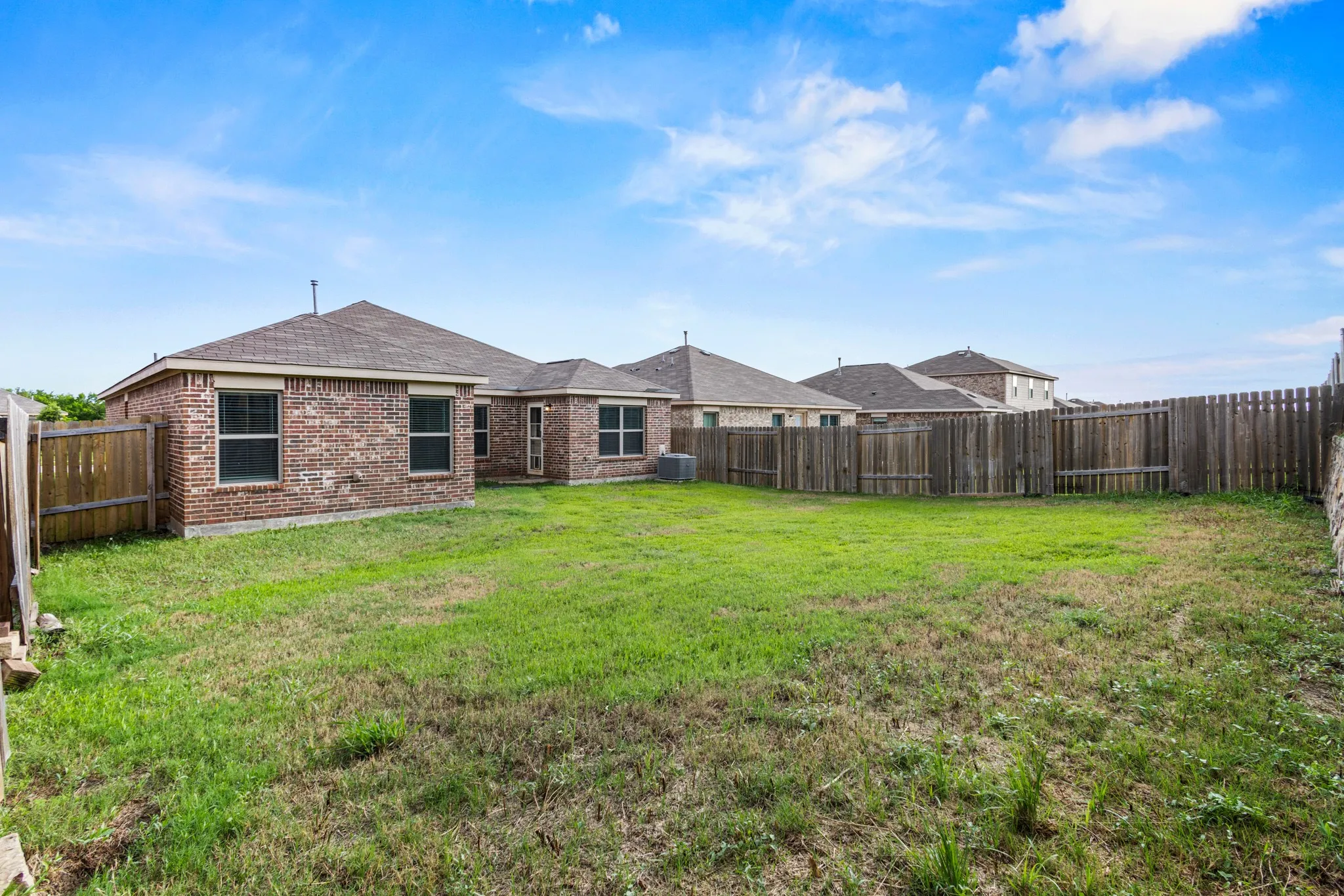 Spacious backyard featuring a substantial lawn area, full privacy fencing, and brick exterior architecture