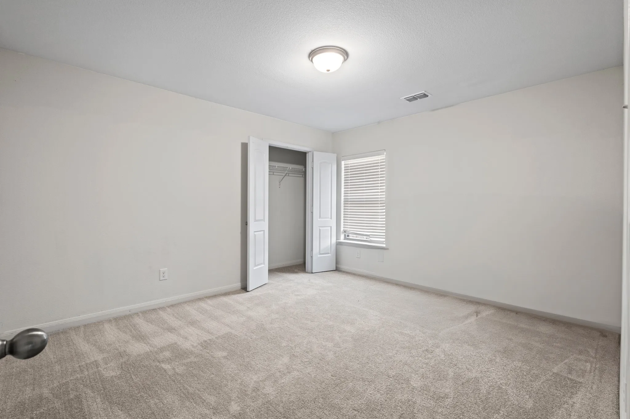 Bright room featuring neutral-toned carpet flooring, a window with horizontal blinds, and a bi-fold door closet with shelving and hanging rods