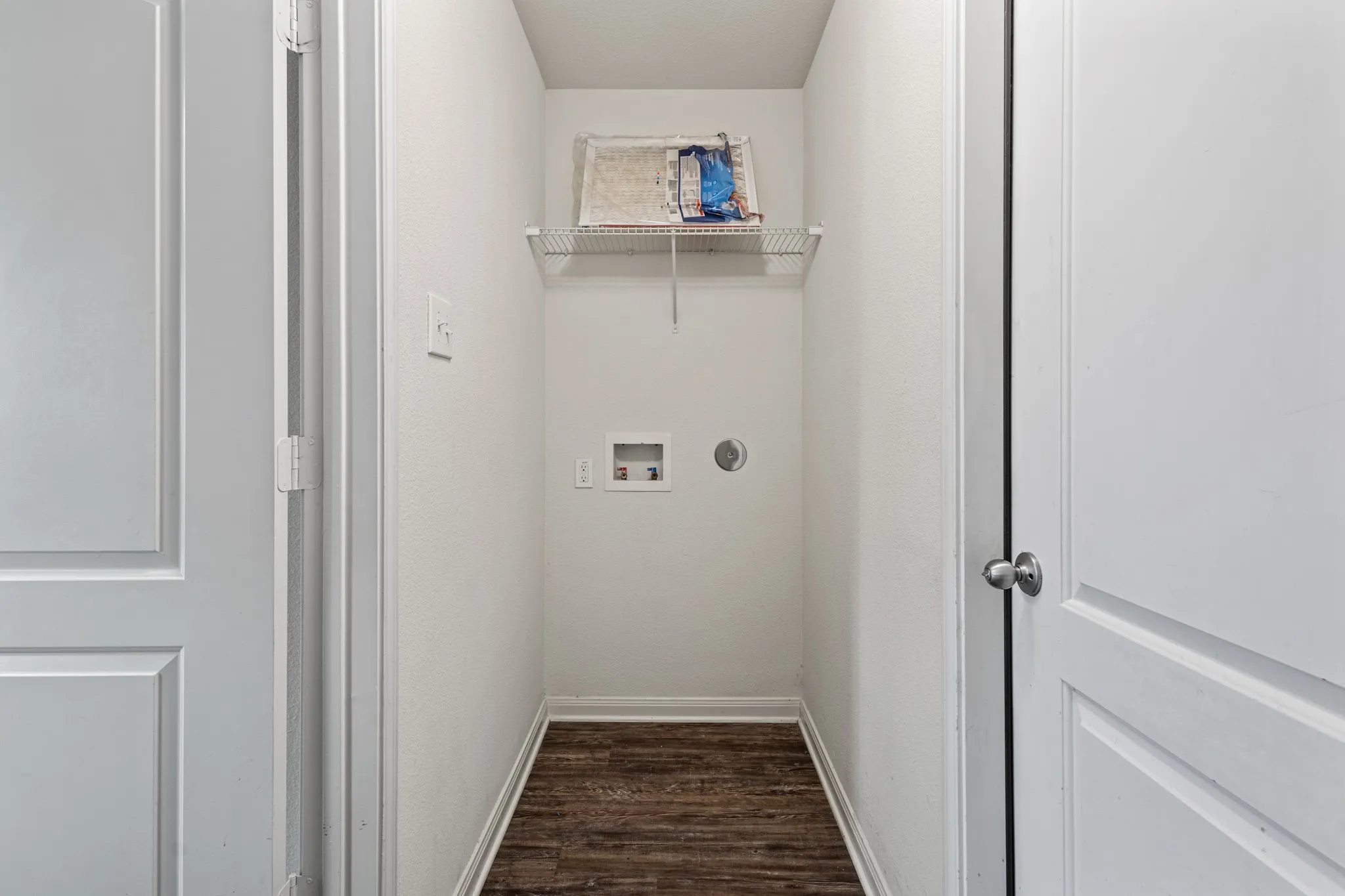 Dedicated laundry area featuring wood-finish flooring, white walls, and a wire storage shelf